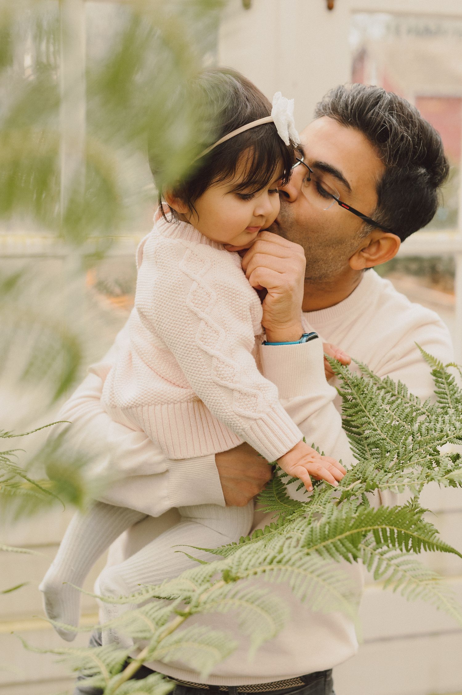 Tender family moment with parent and child among greenery and ferns.