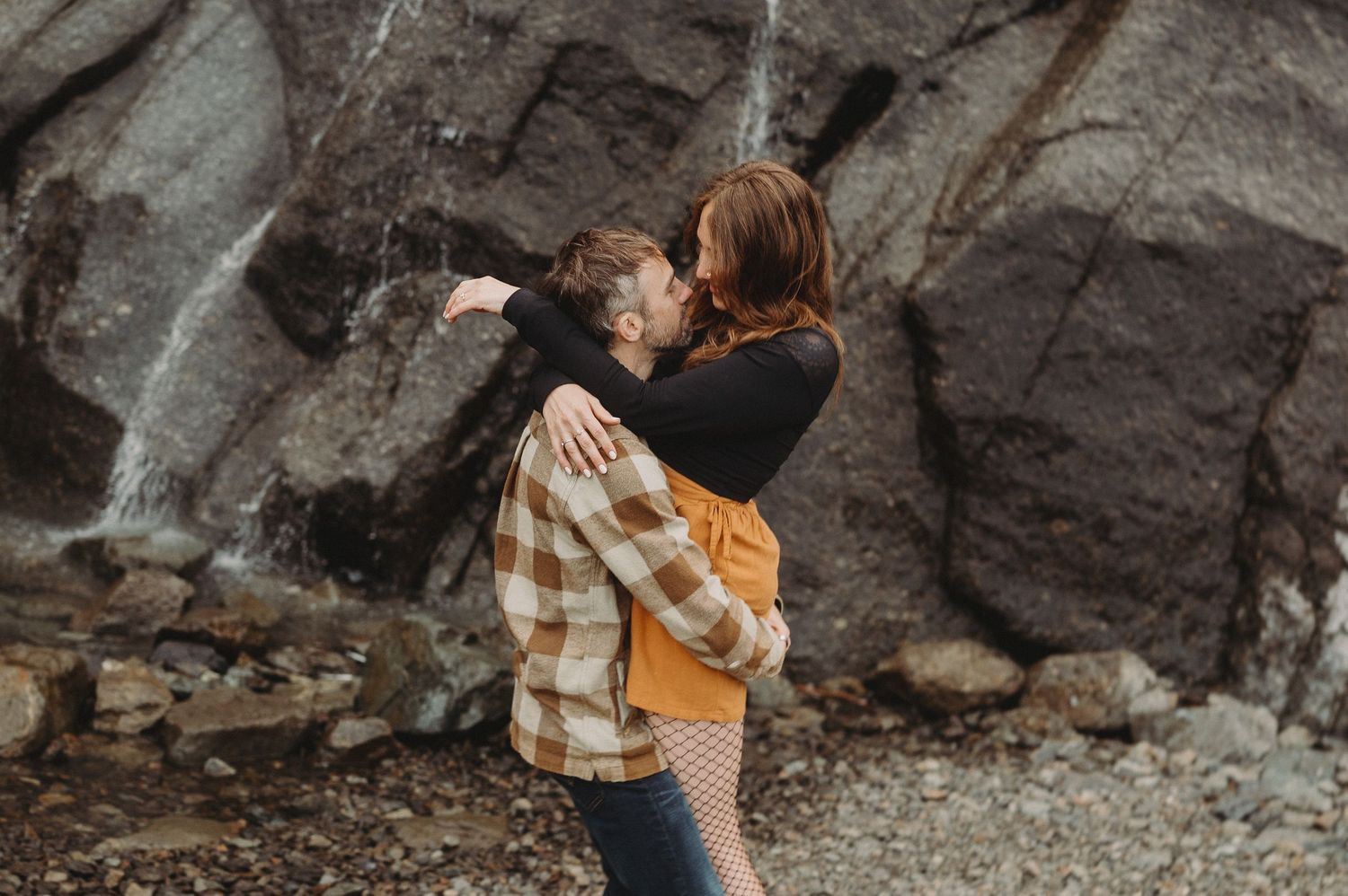 Couple in romantic embrace photographed against rocky cliffs at sunset in warm golden light.