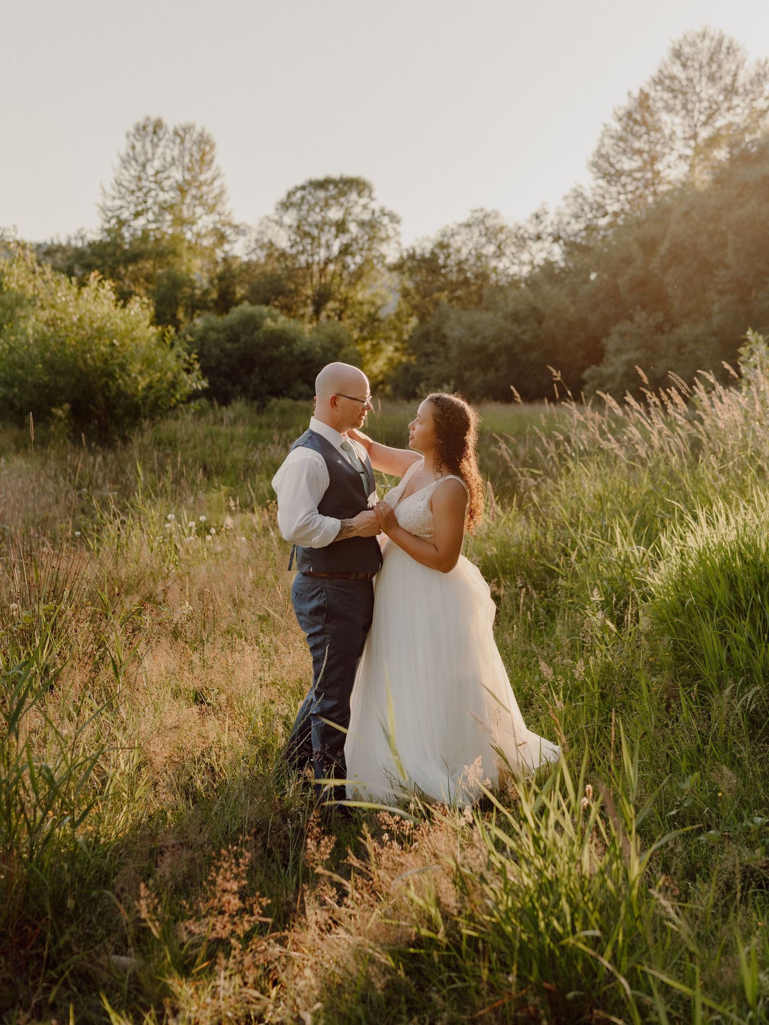 A romantic sunset wedding photo of a couple dancing in a field of tall grass and wildflowers.