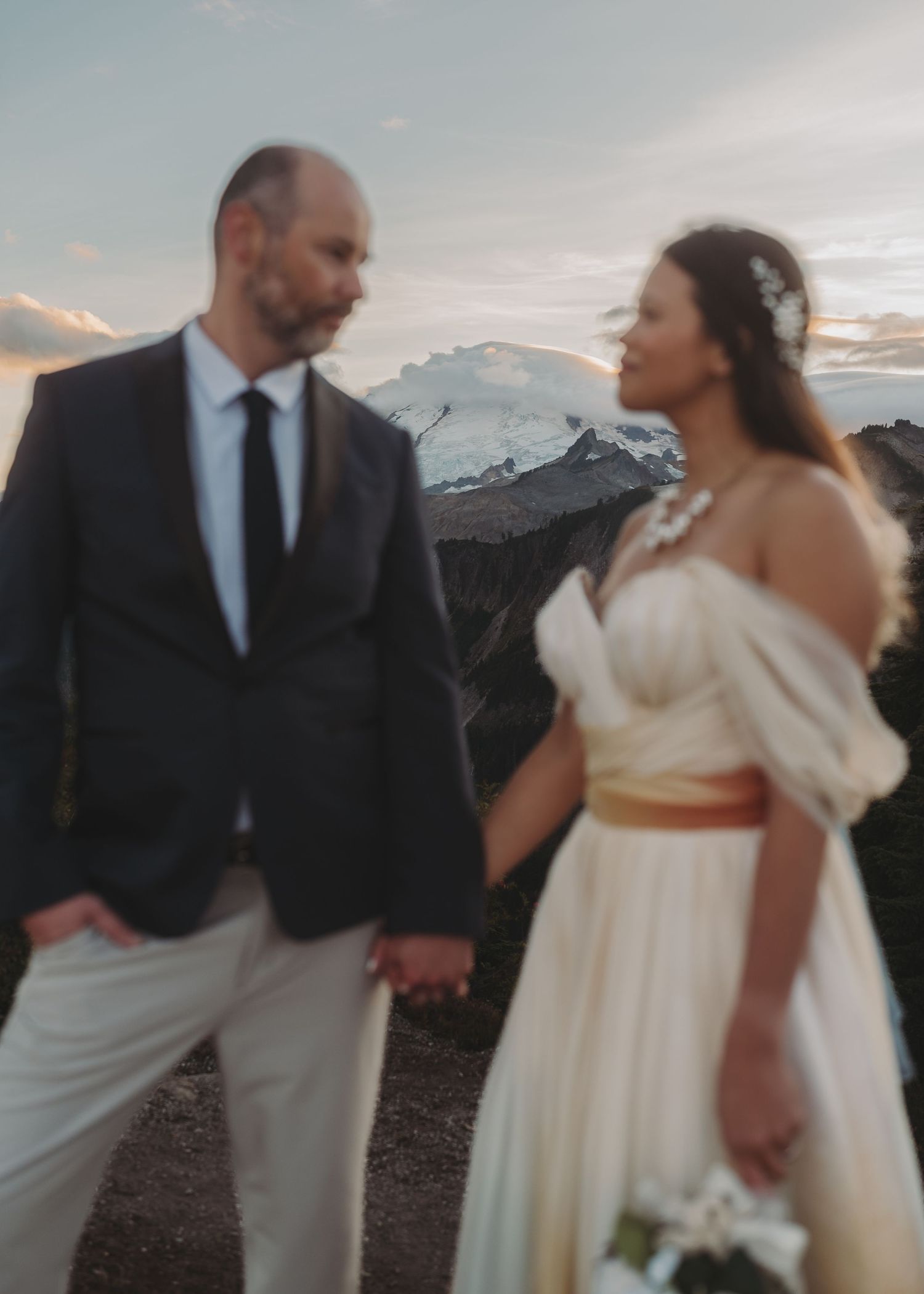 A couple shares an intimate moment in formal attire against a mountainous backdrop.