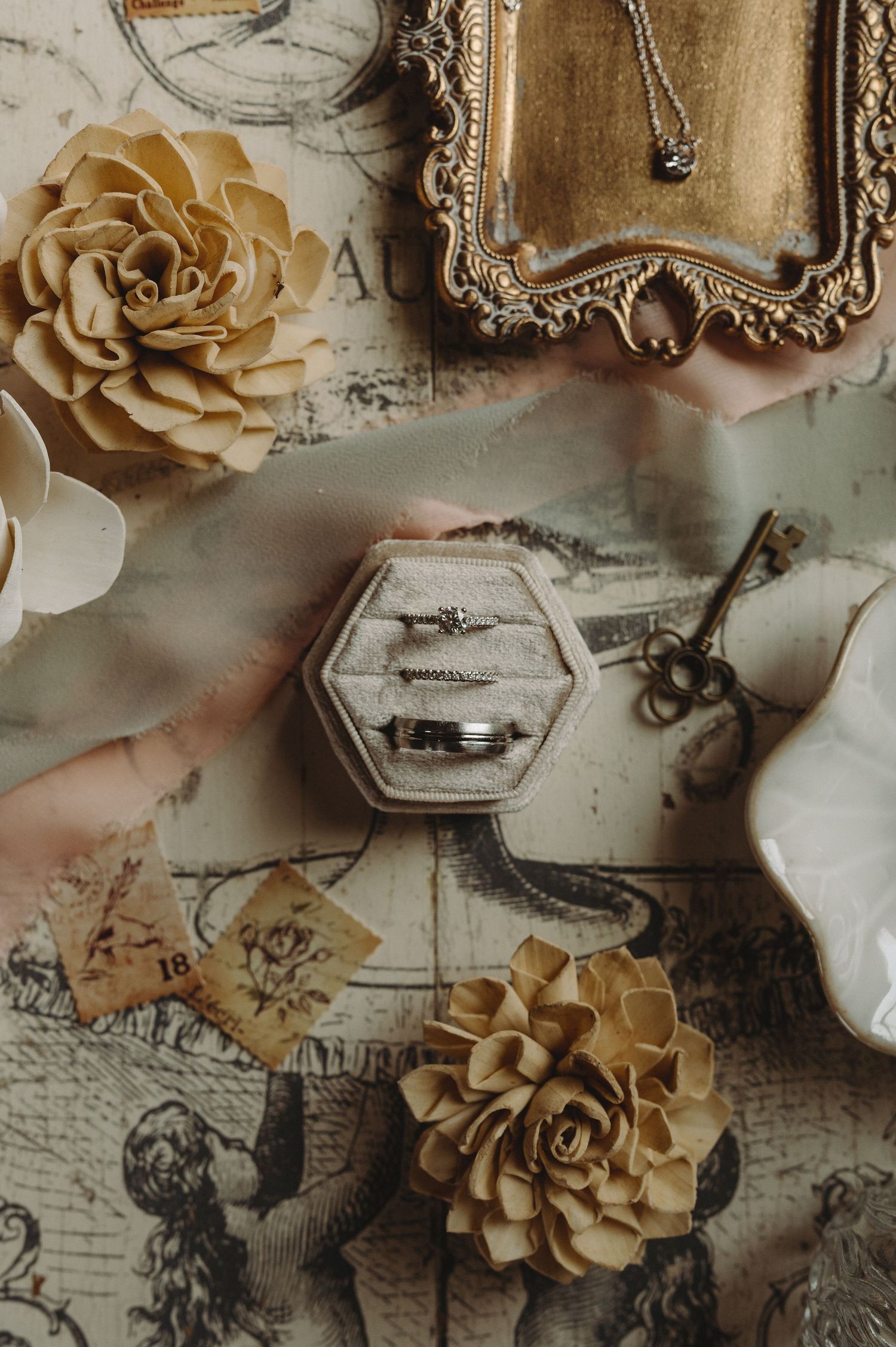 Vintage-style flatlay with gold roses, an ornate frame, and a hexagonal ring box on antique paper.
