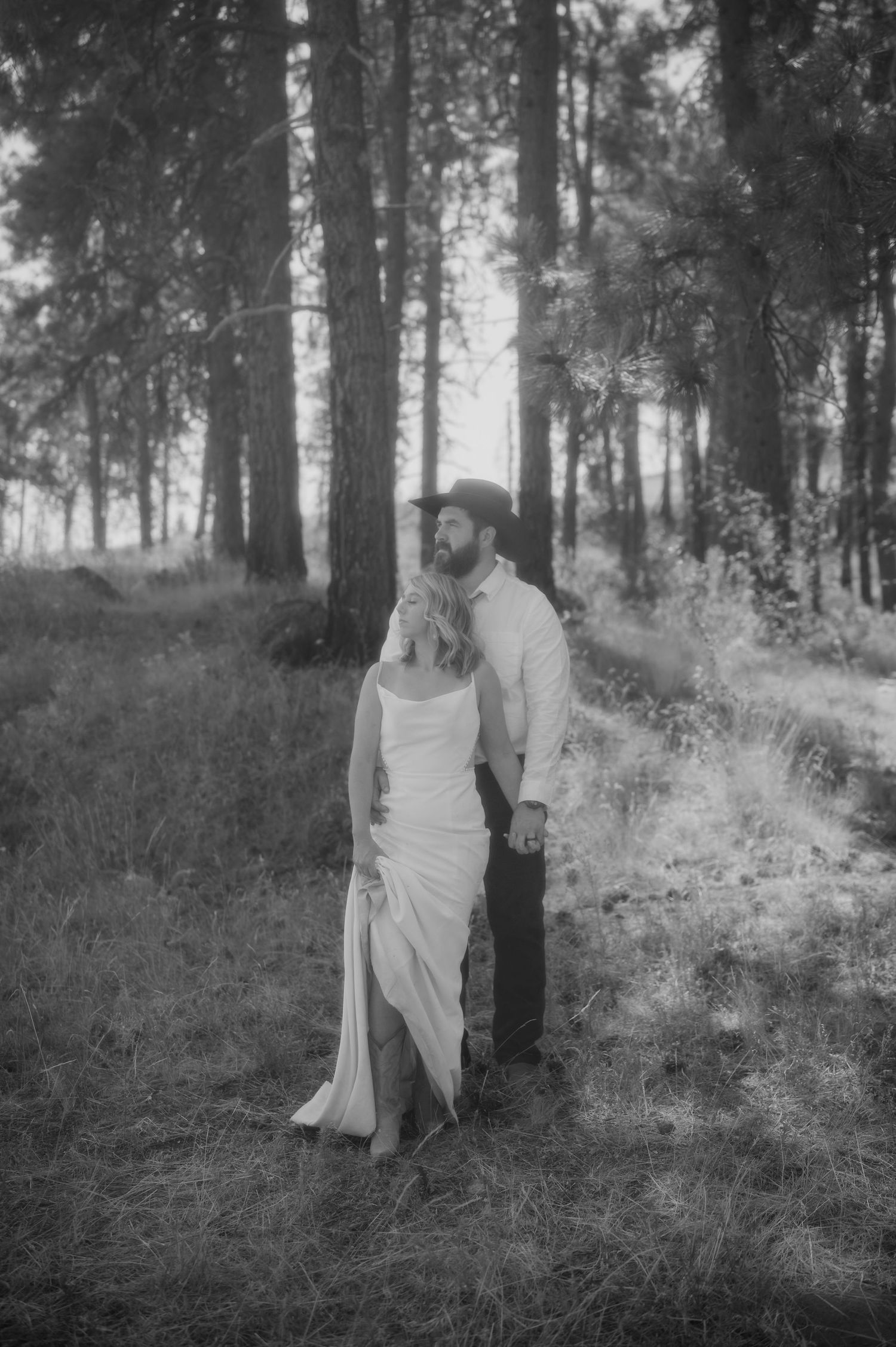 A black and white photo of a couple standing together in a misty forest setting.