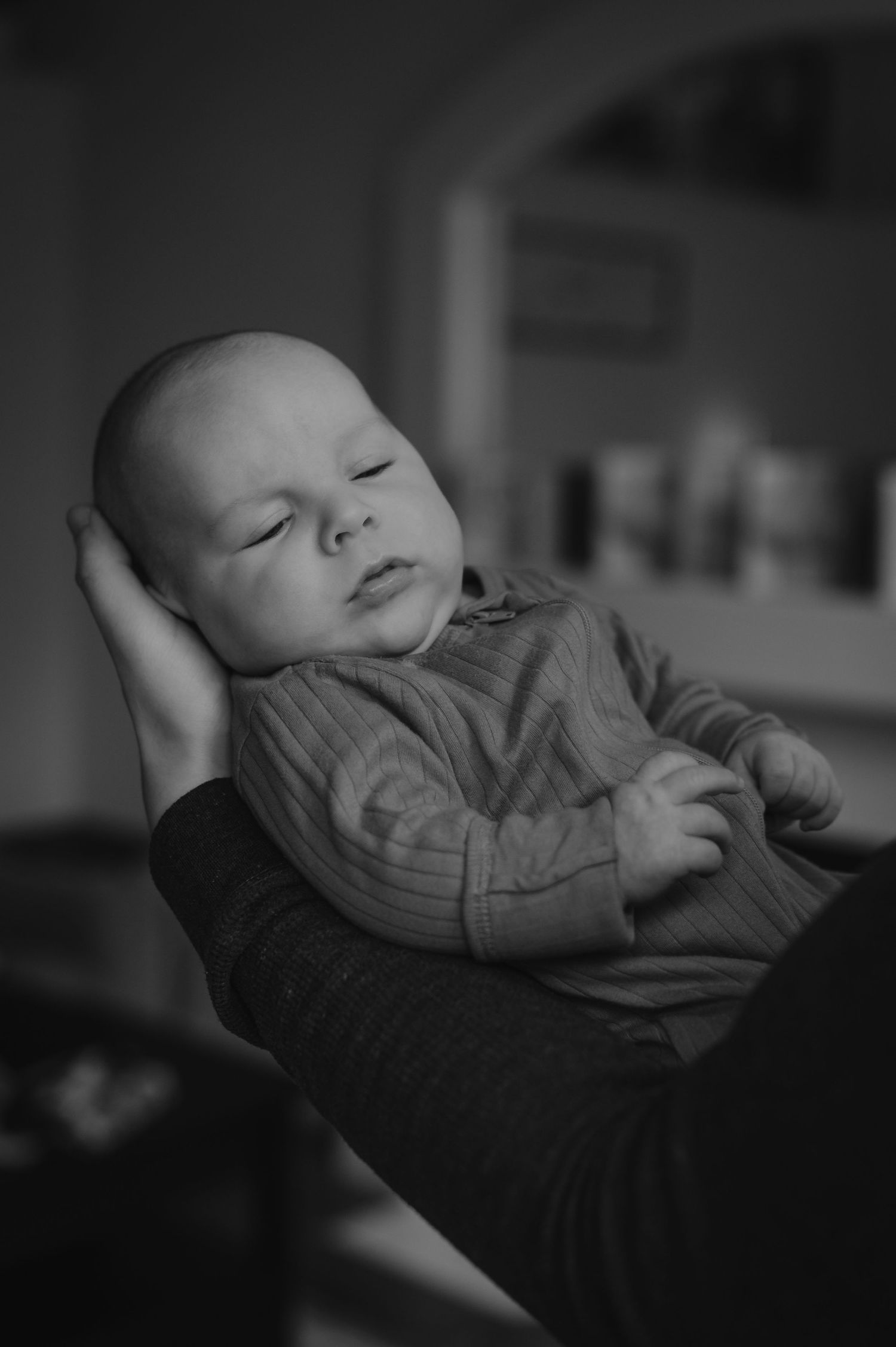 Black and white photo of a sleeping newborn baby cradled in an adult's arms, wearing a striped onesie.