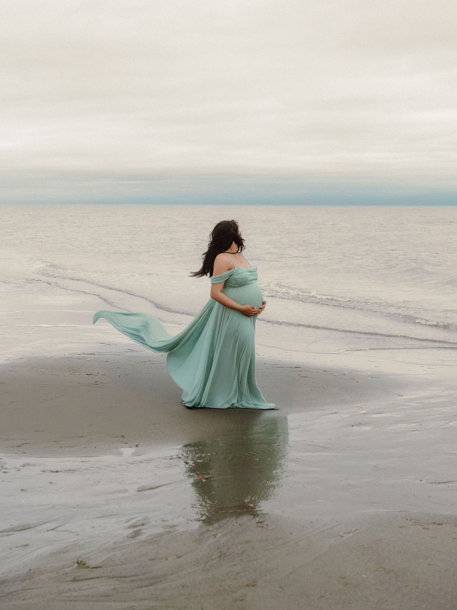 A figure in a flowing mint green dress twirls gracefully on a misty beach, creating an ethereal seaside scene.