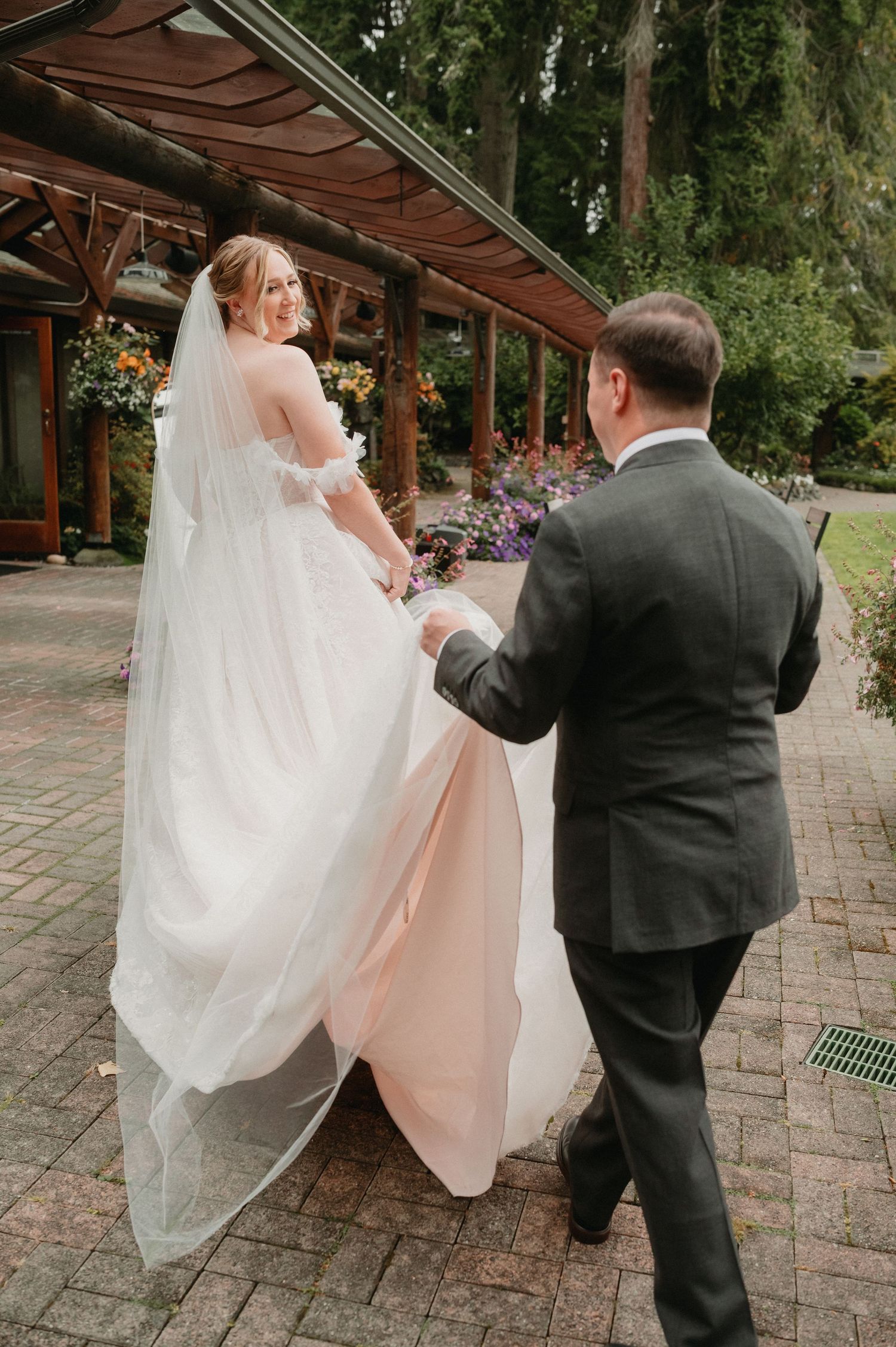 Couple dressed in formal wedding attire sharing a playful moment while walking on brick pavers under covered walkway.
