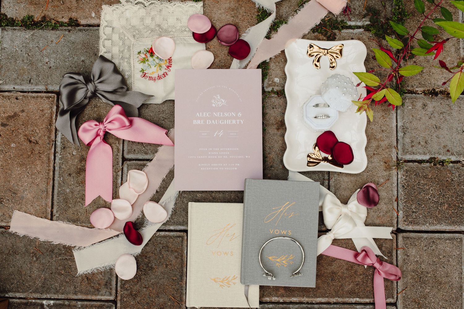 Wedding stationery and decor items in pink and burgundy tones arranged on a rustic stone surface.
