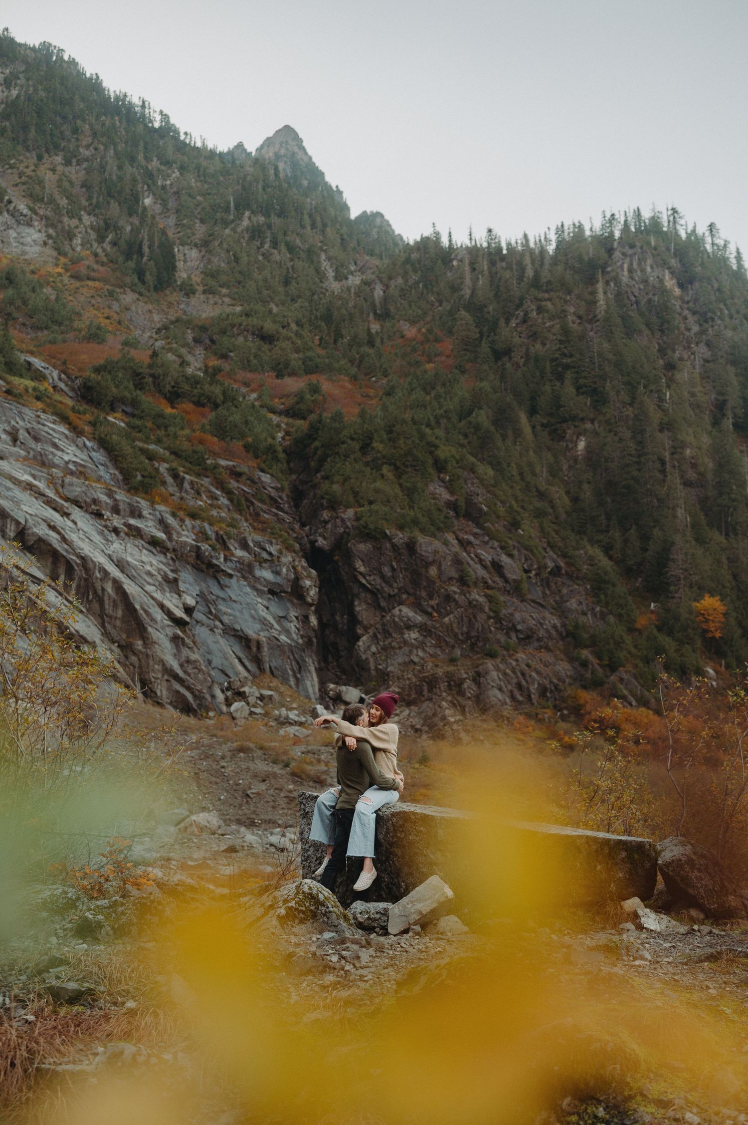 A distant figure sitting on rocky terrain with mountainous landscape in the background.