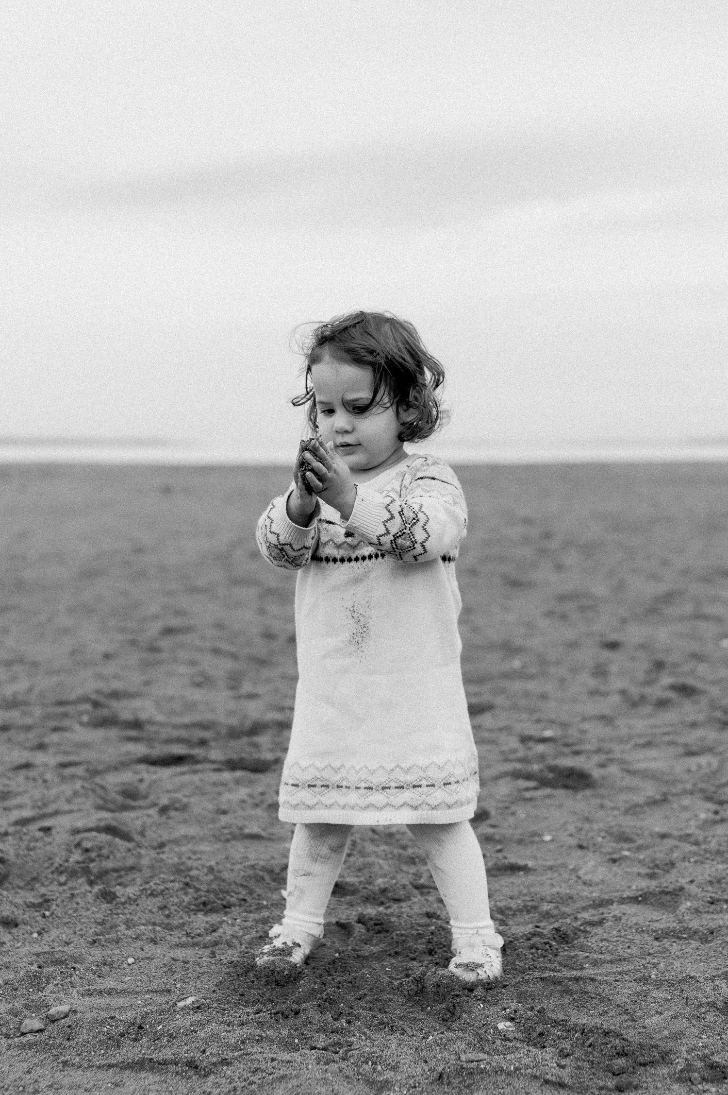 Young child in white dress playing on a misty beach.