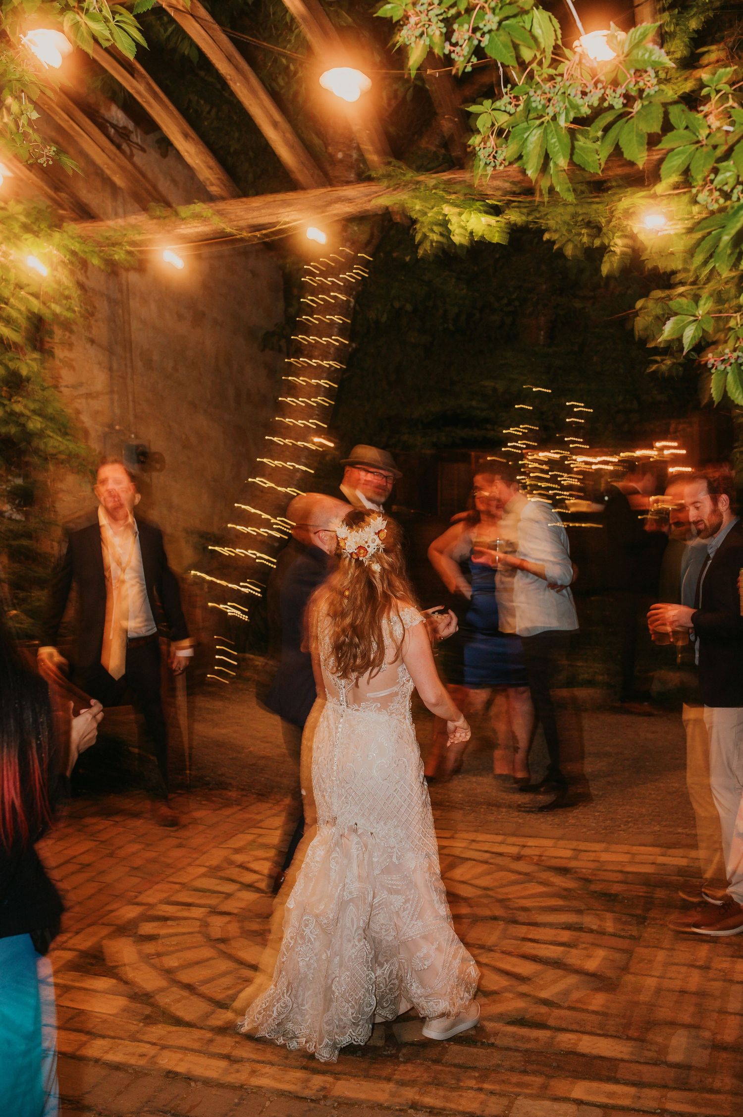 Wedding reception dance party under string lights with guests in motion.