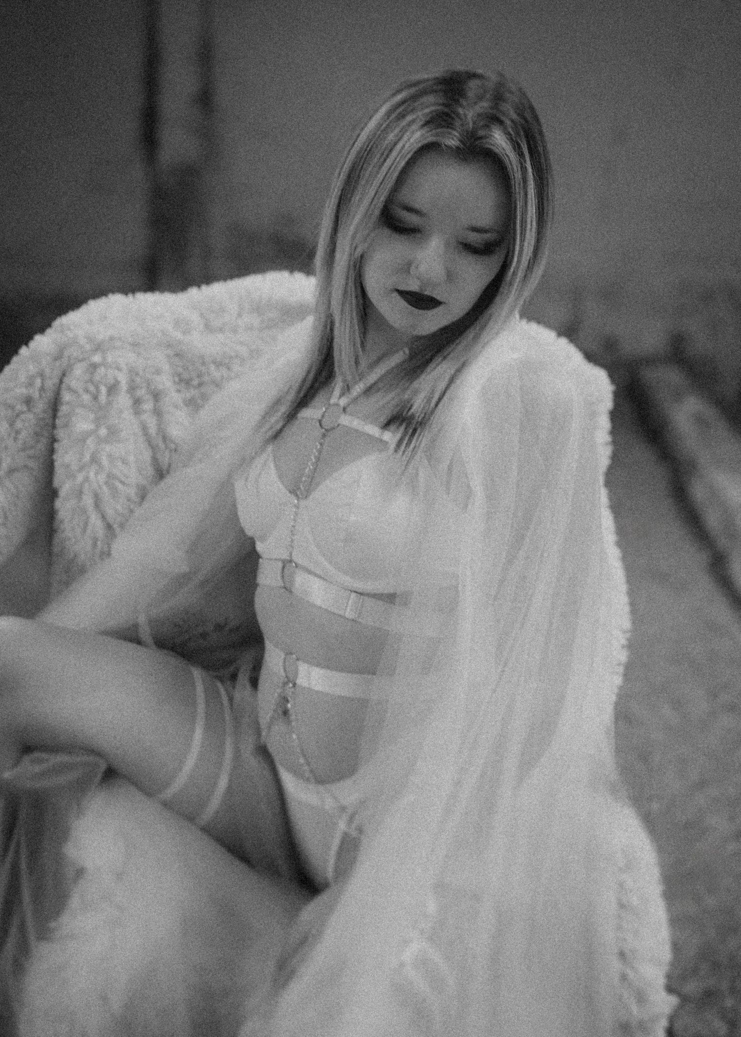 A woman wearing white lace lies on cream-colored fabric in a black and white artistic boudoir photo series.