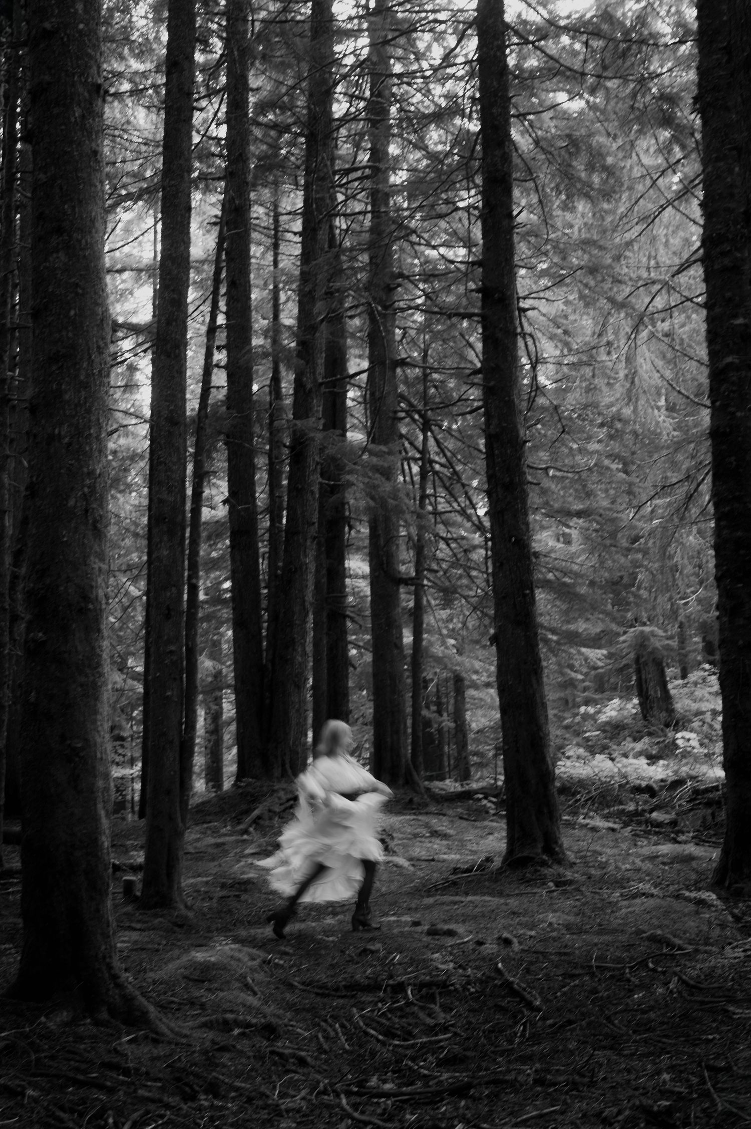 Blurred figure in white dress running through dark forest with tall trees, black and white photography.