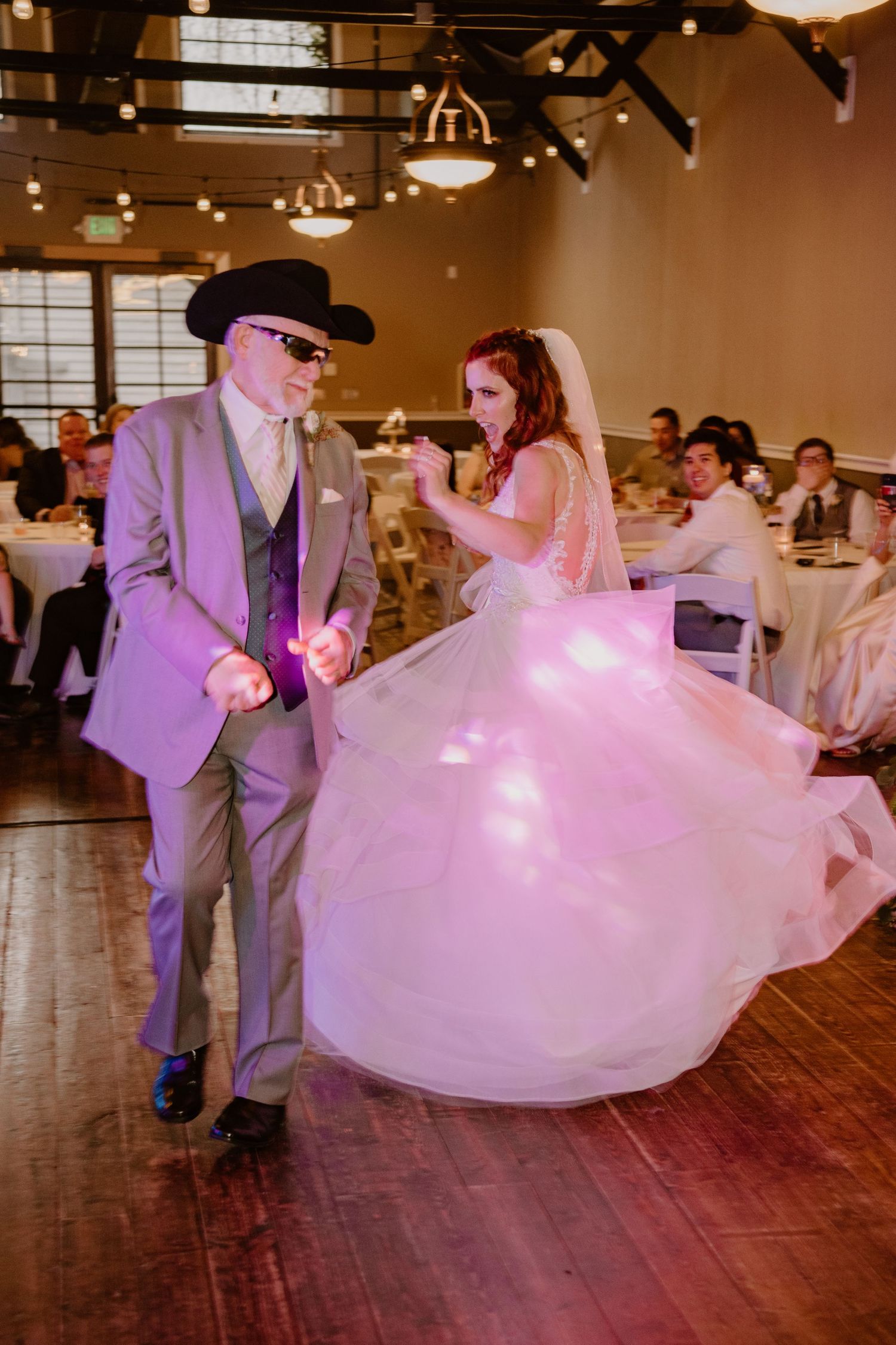 A couple dancing at their wedding reception, with the bride's white dress twirling on a wooden floor.