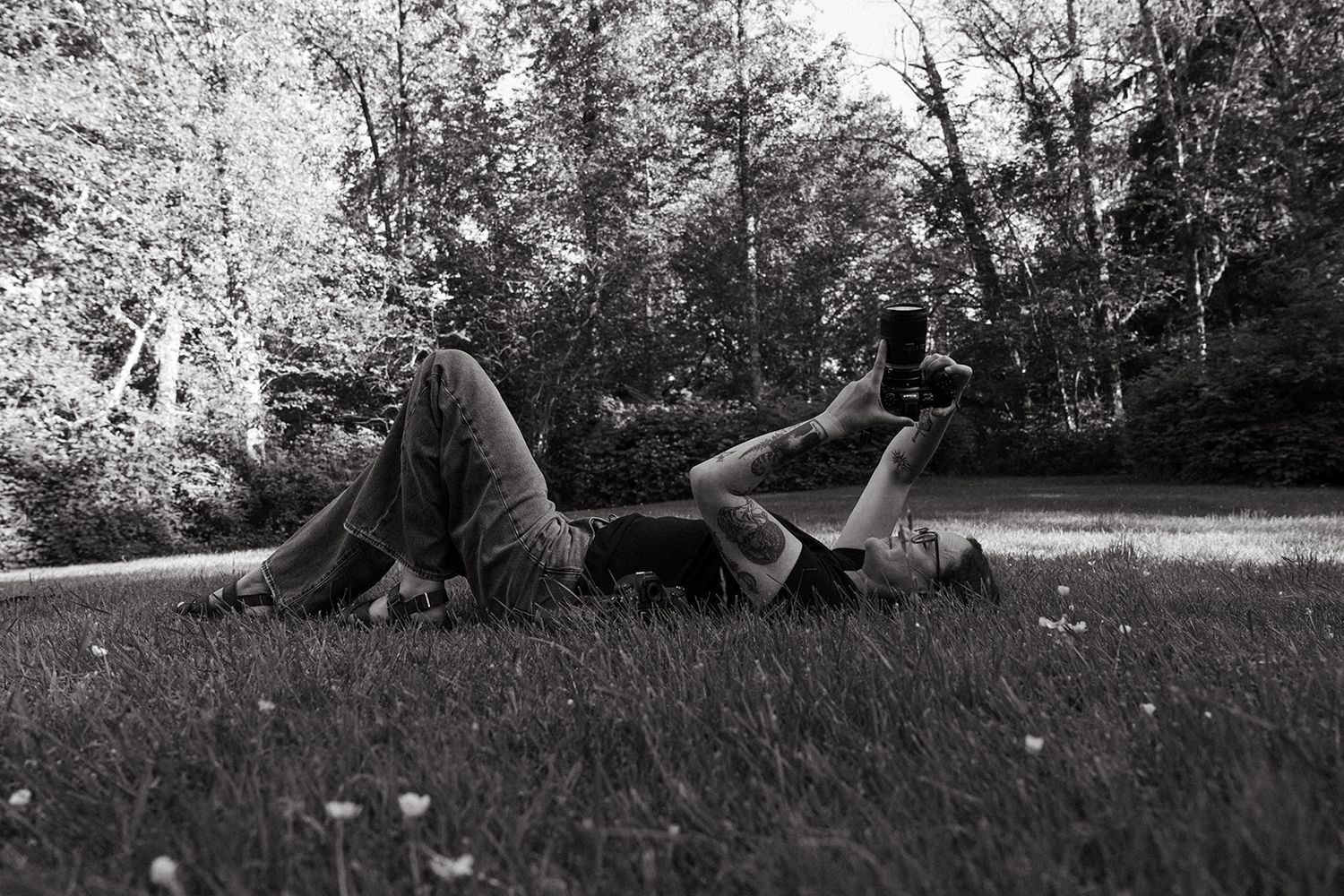 Black and white photo of two people lying on grass in a park, relaxing outdoors surrounded by trees.