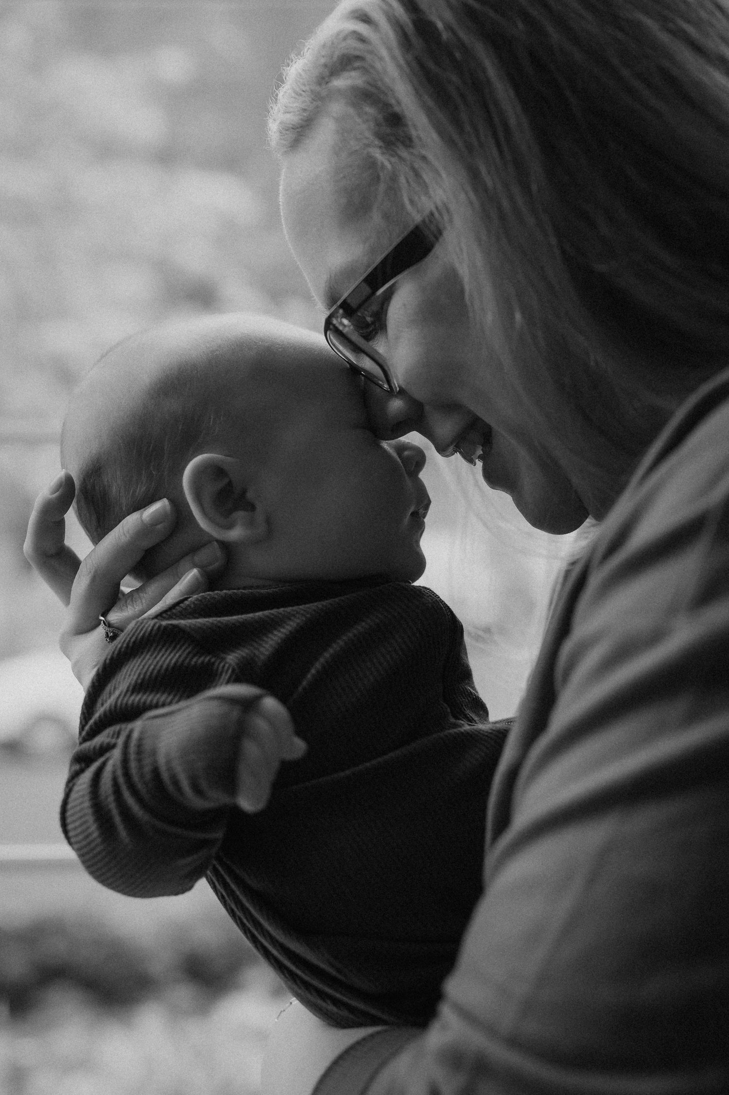 Black and white photo of a smiling woman with glasses tenderly holding and nuzzling a newborn baby.
