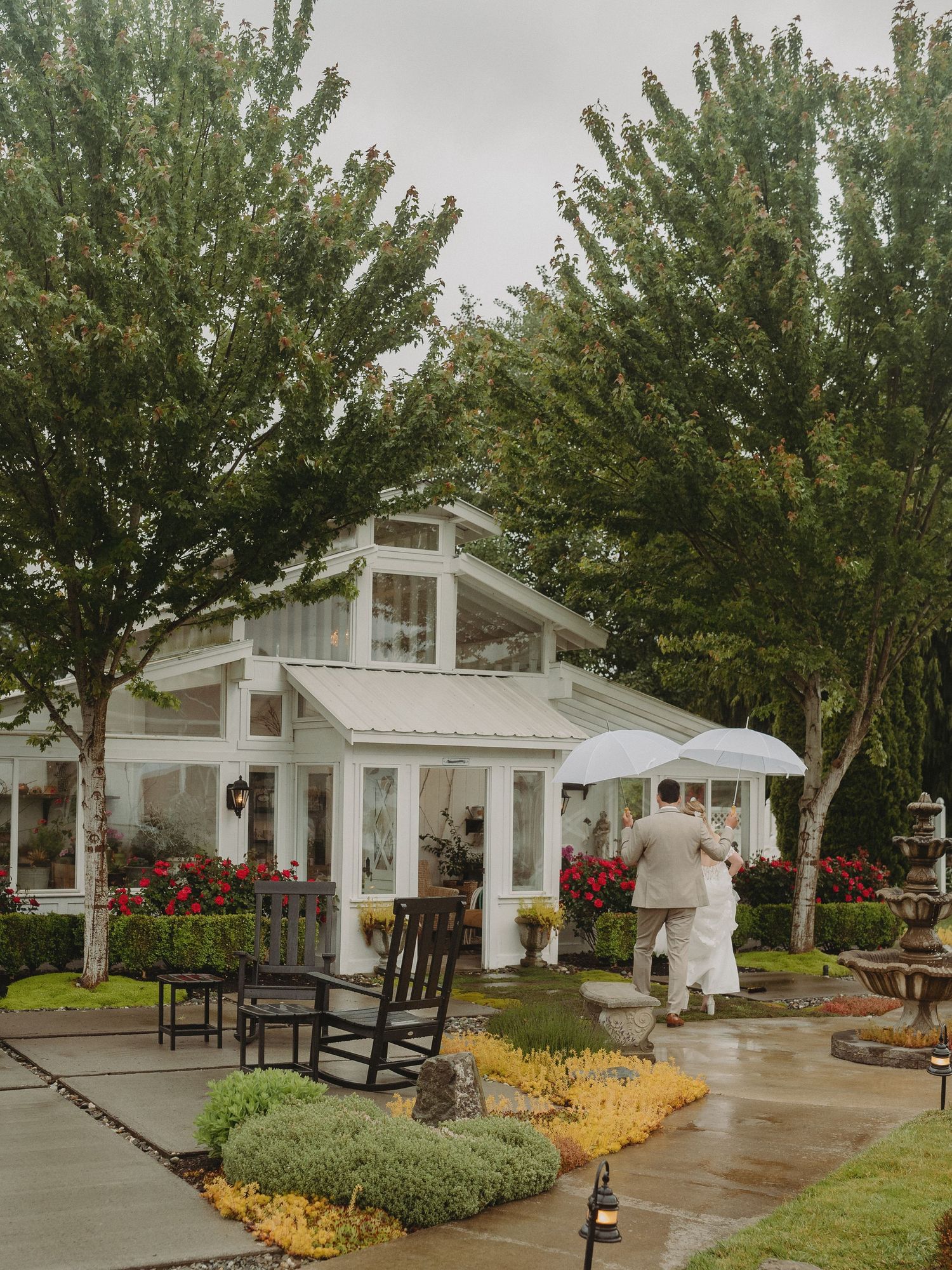 A white wedding venue with rocking chairs and flowering trees on a cloudy day.