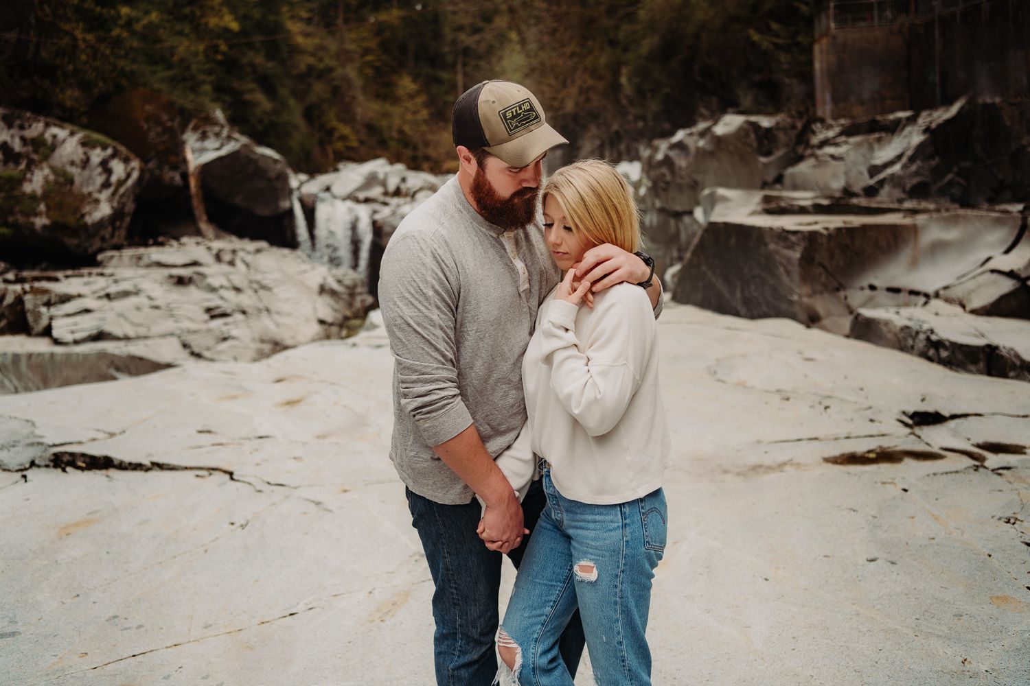Couple embracing and laughing together on a rocky terrain near a waterfall.