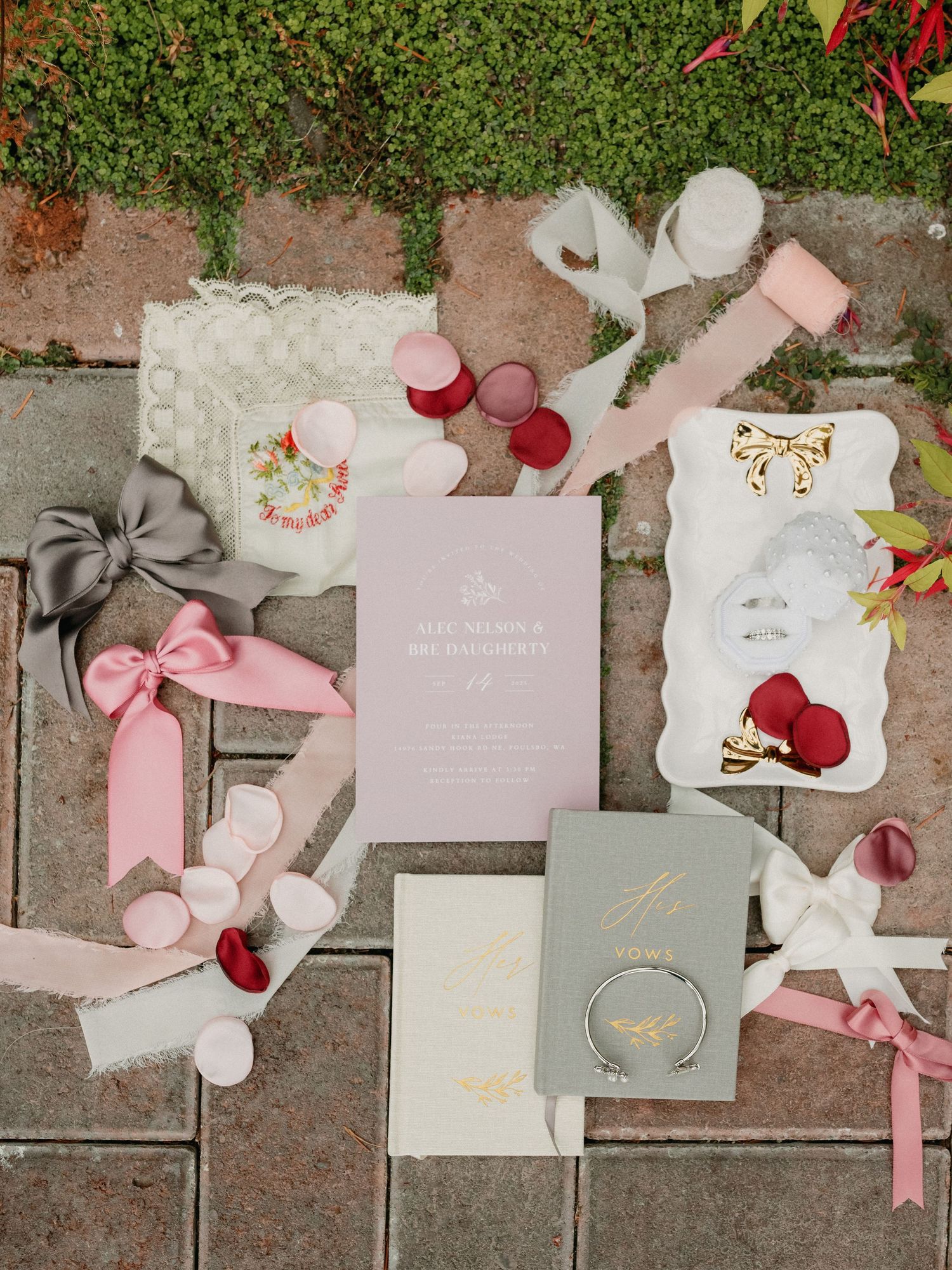 Elegant wedding stationery flatlay with pink and gray invitations, envelopes, and floral details on stone paving.