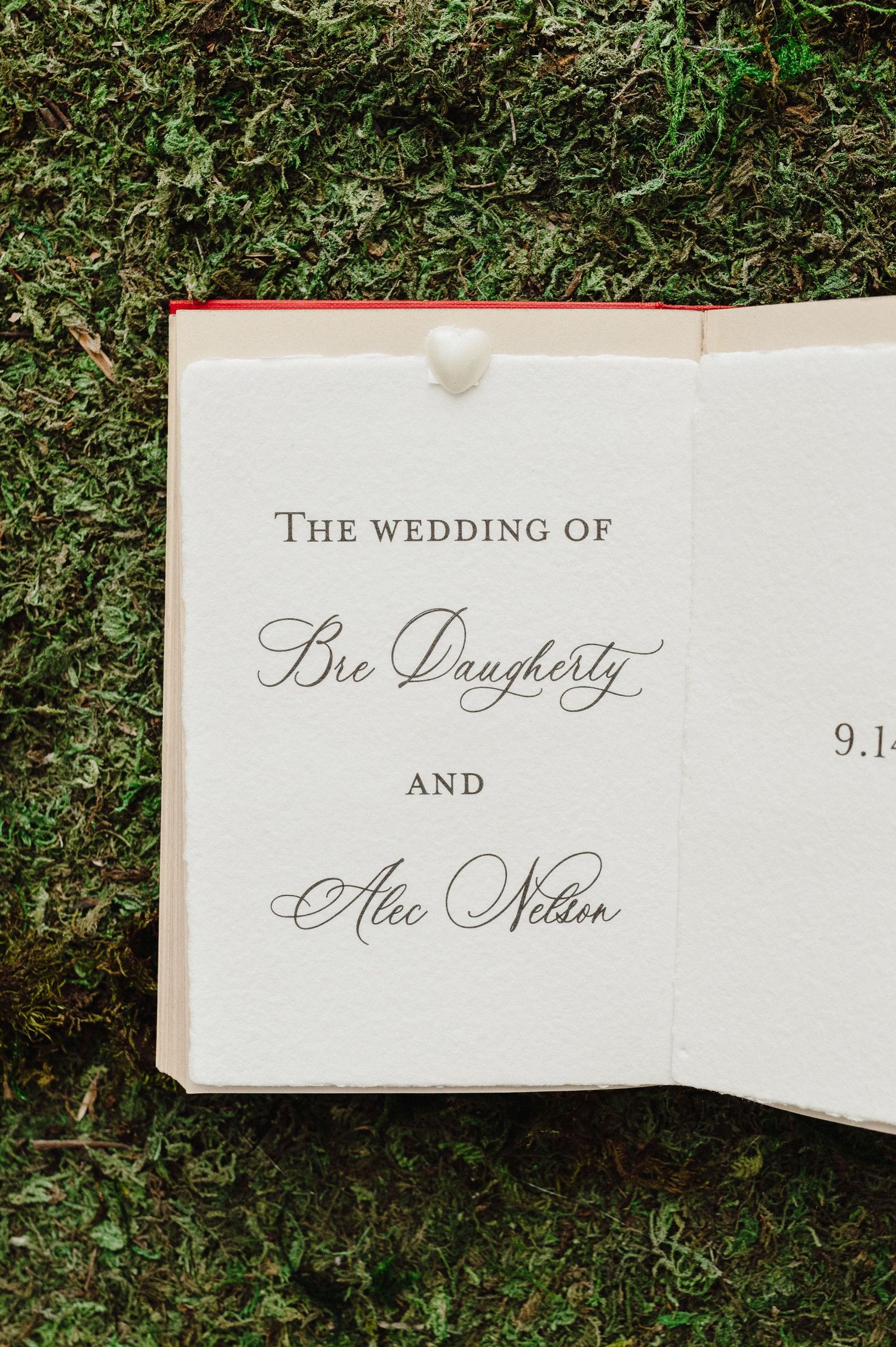 Wedding invitation cards with elegant calligraphy text laid on green grass background.
