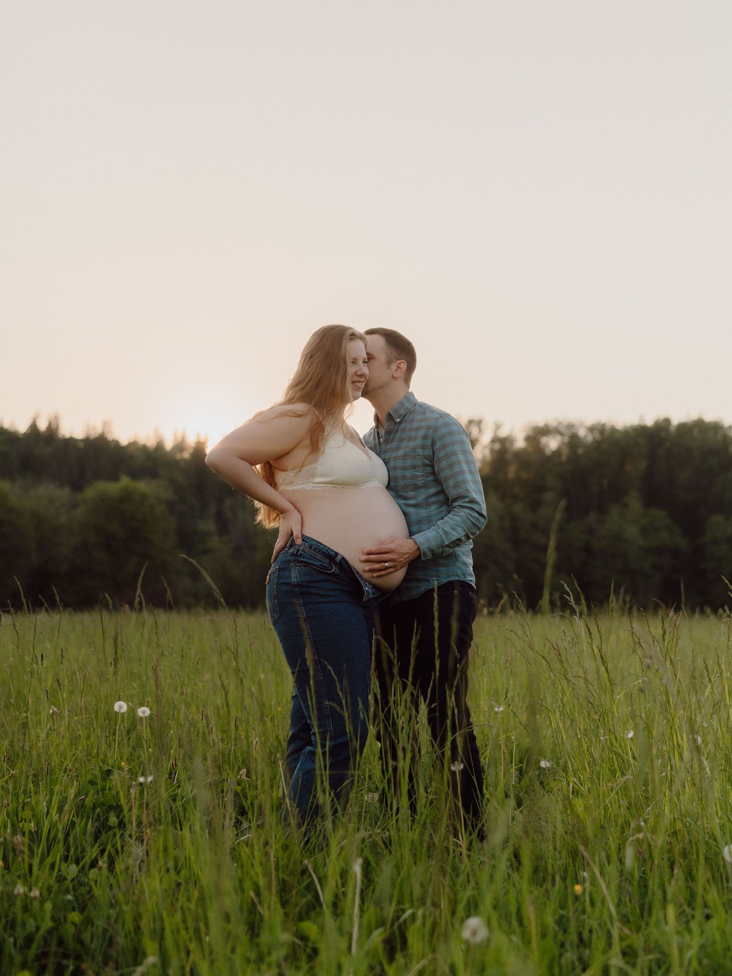 Couple sharing intimate moment in field during sunset maternity photo session.