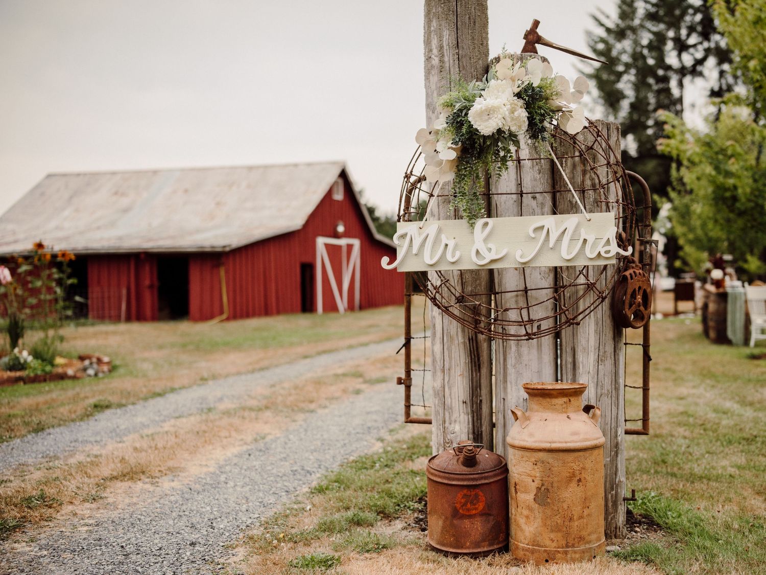Rustic wedding decor with vintage lanterns and florals near a red barn in the countryside.