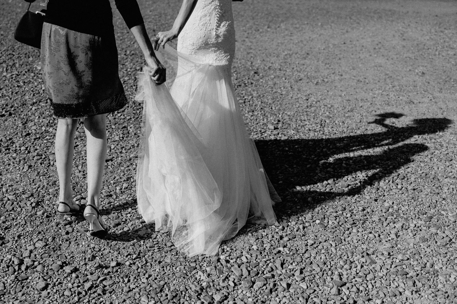 Black and white photo showing shadows of a couple walking on gravel in wedding attire.