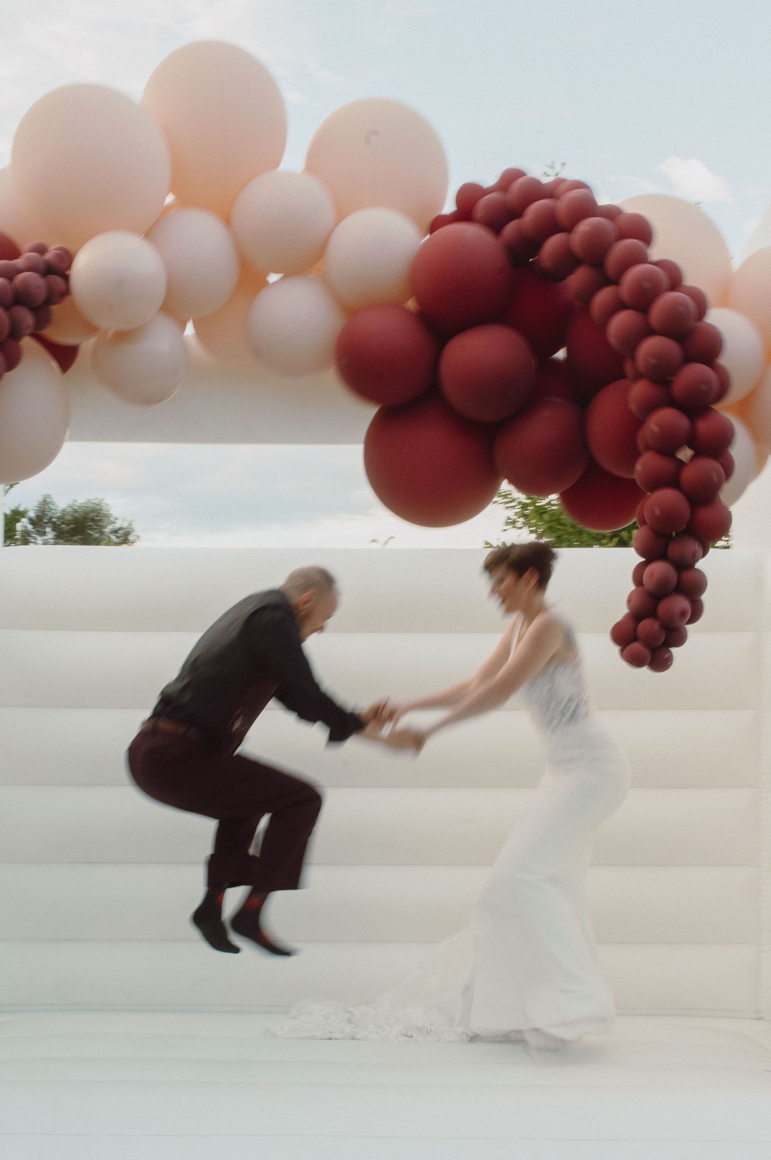 Wedding couple dancing under an elegant balloon arch with white and burgundy balloons.