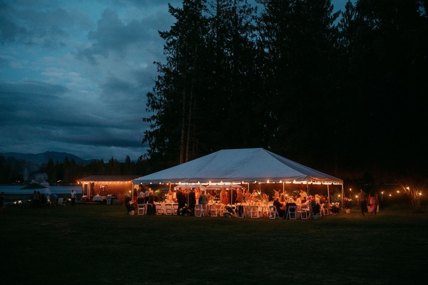 An illuminated wedding tent glows against a dramatic dark blue evening sky with string lights creating a warm ambiance.