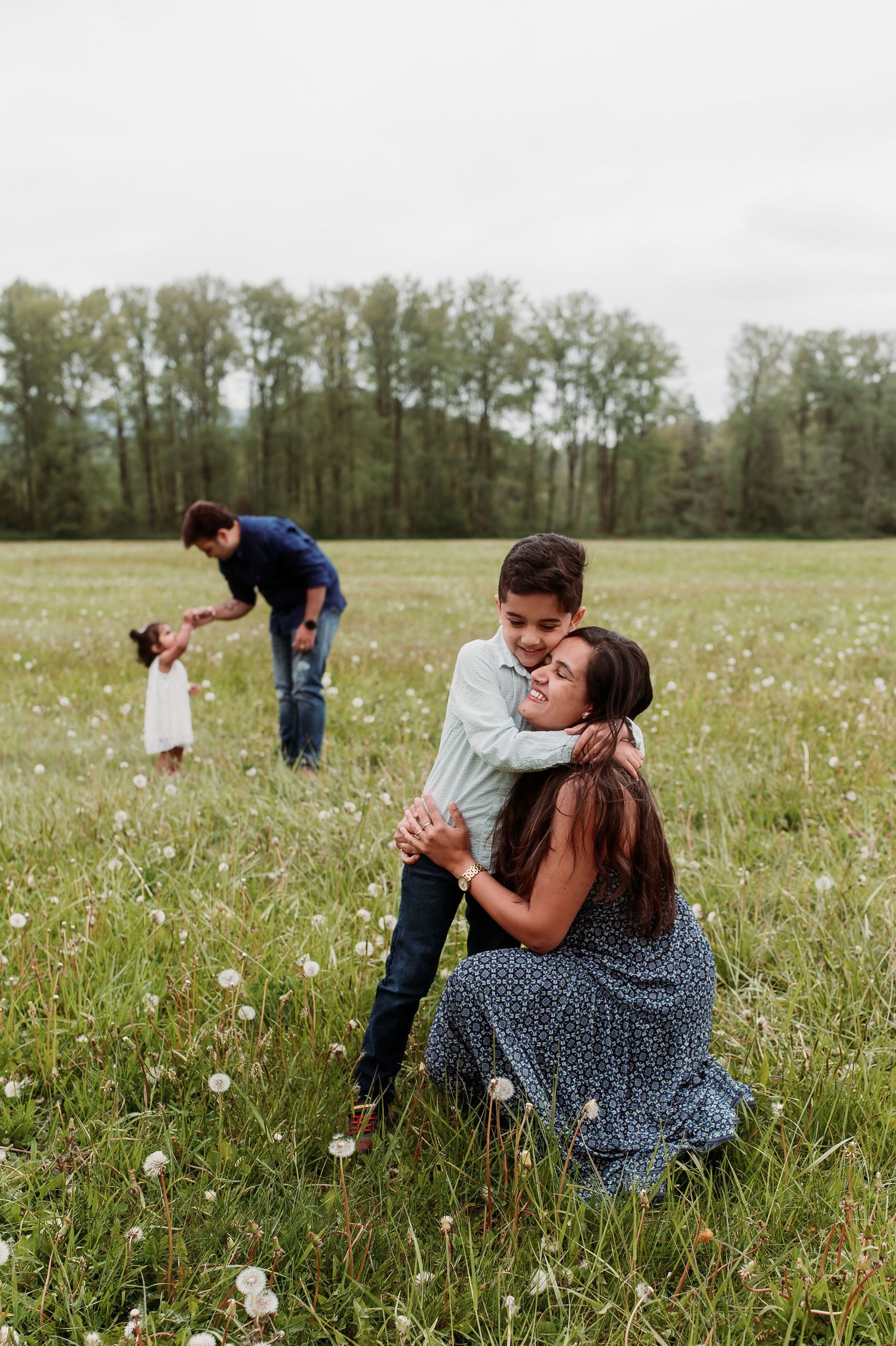 People enjoying a spring day in a wildflower meadow surrounded by tall trees in the distance.
