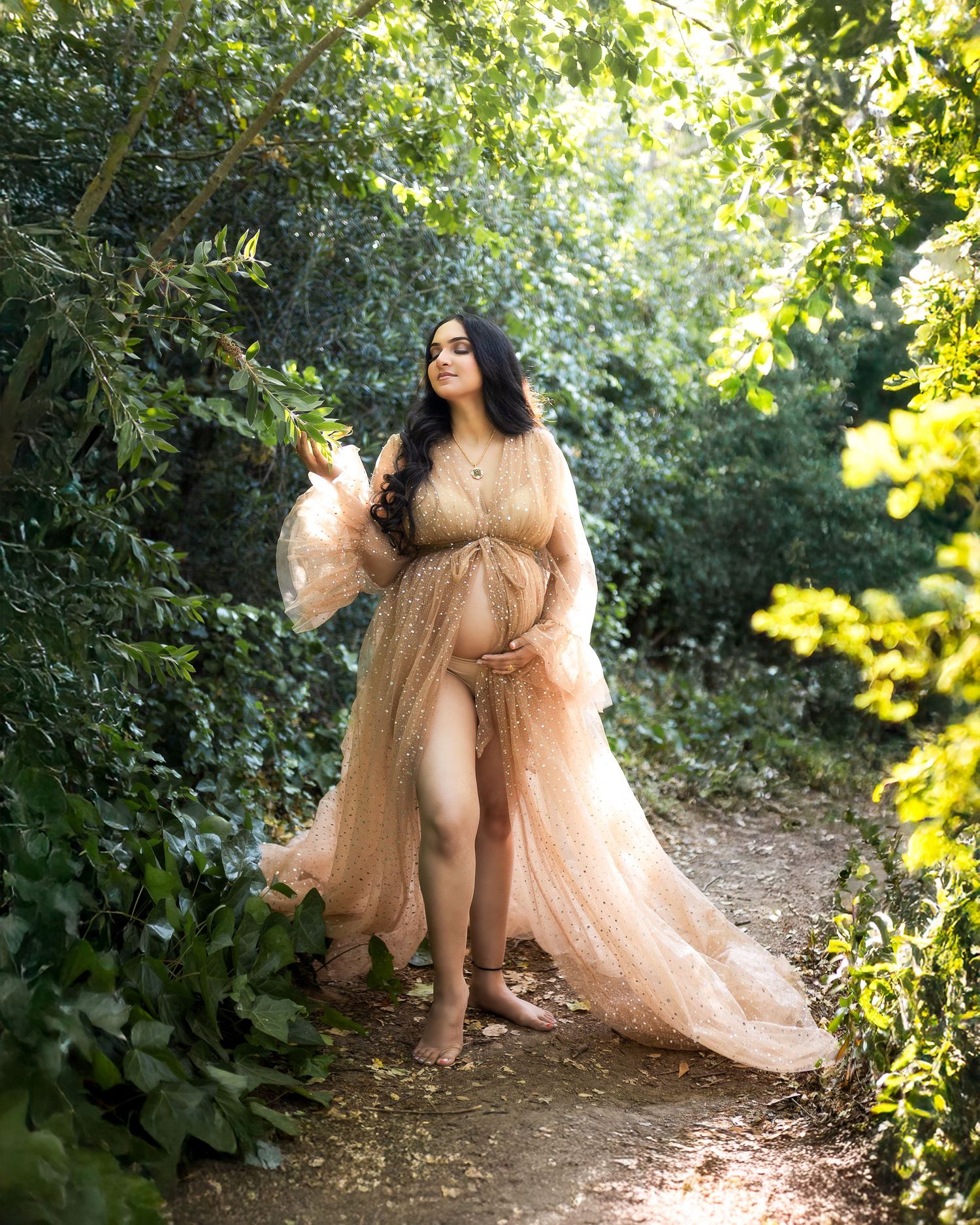 A dreamy outdoor photoshoot features a champagne-colored tulle gown against a lush green forest backdrop.