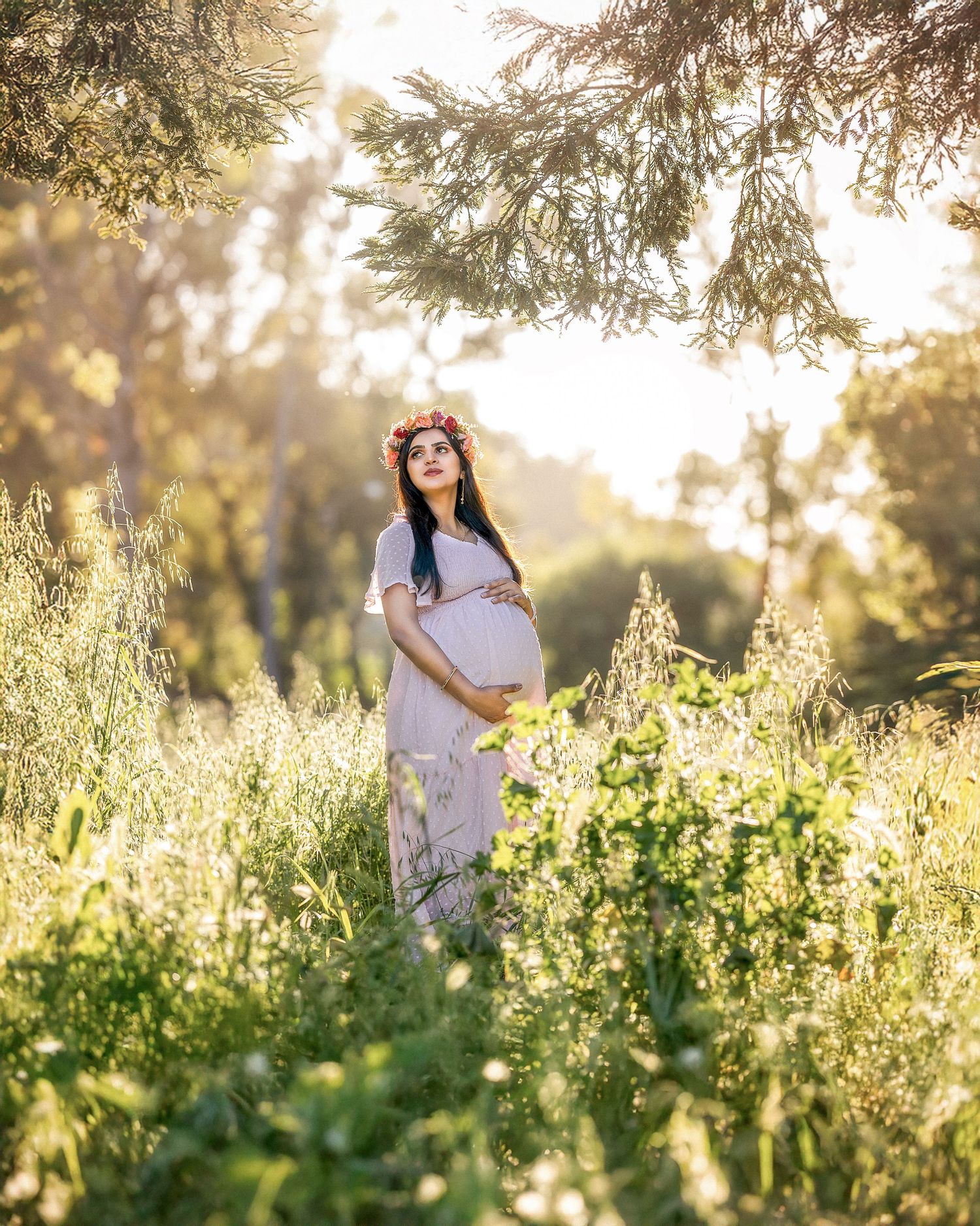 A person in white clothing stands among wildflowers in a sunlit meadow during golden hour.