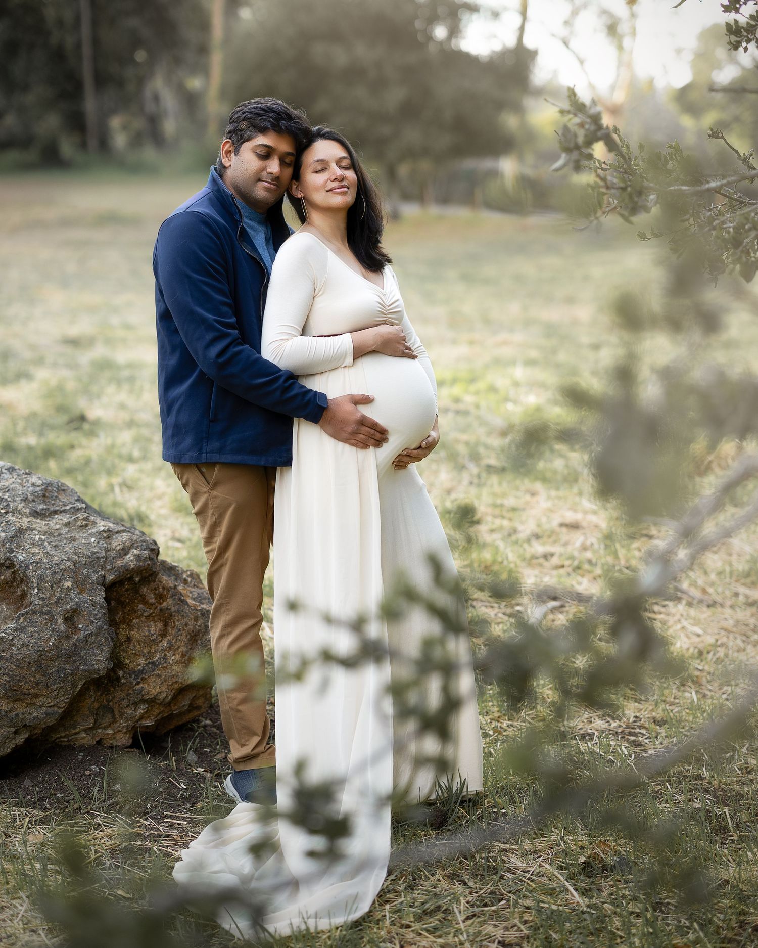 A couple in a natural outdoor setting shares an intimate maternity photography moment against a soft blurred background.