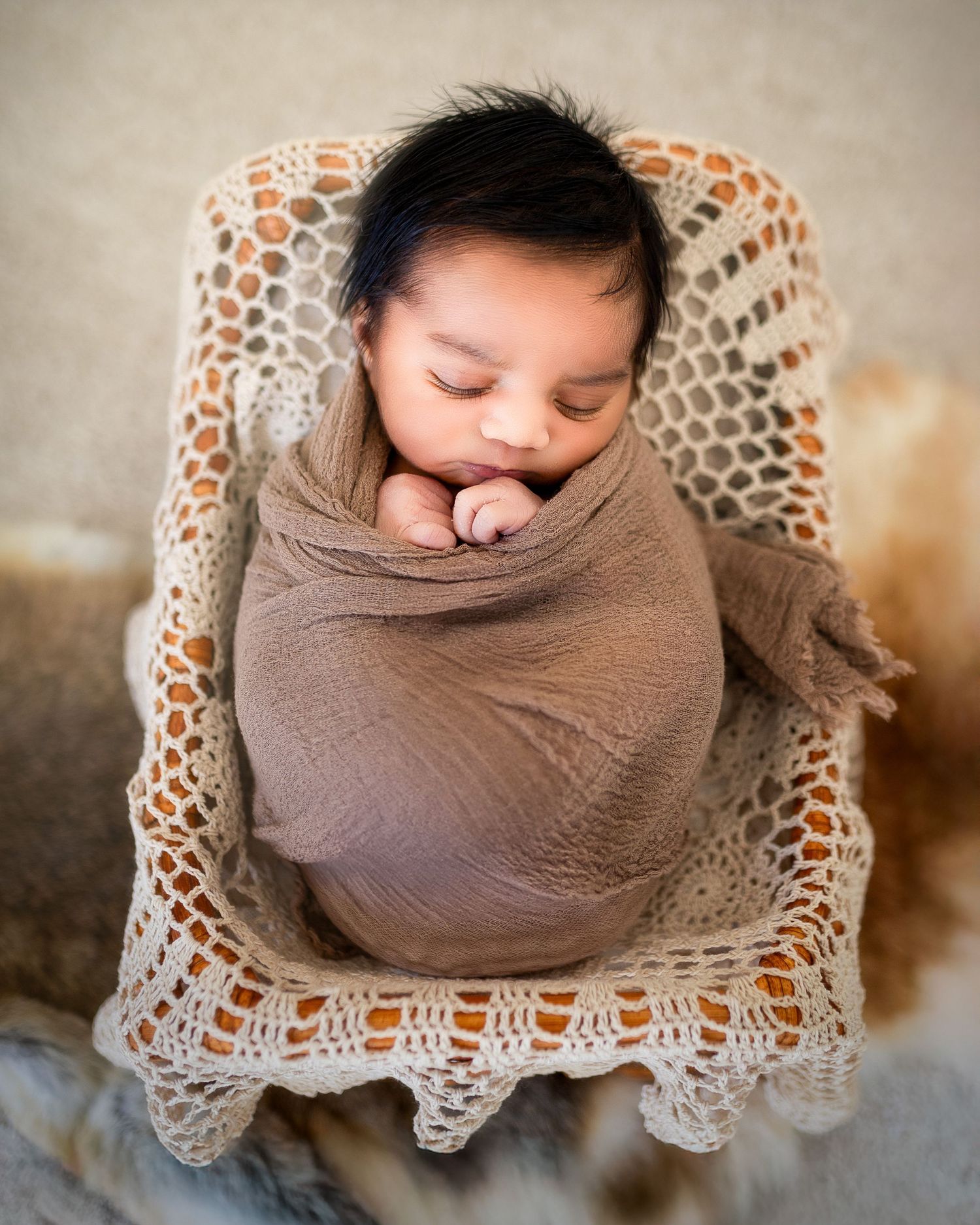 A series of newborn photography shots showing a baby swaddled in brown fabric on a delicate lace doily background.