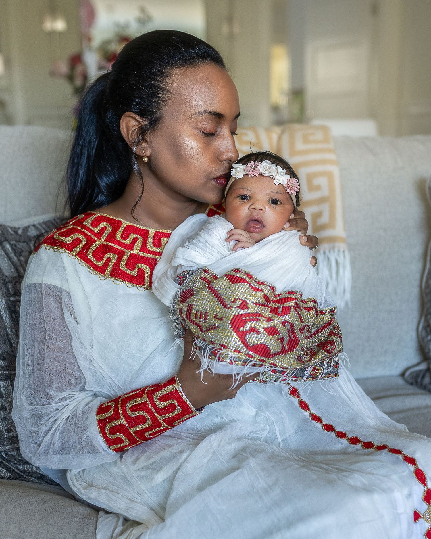 A series of tender moments showing a parent in white clothing and red scarf holding and kissing a baby in white.