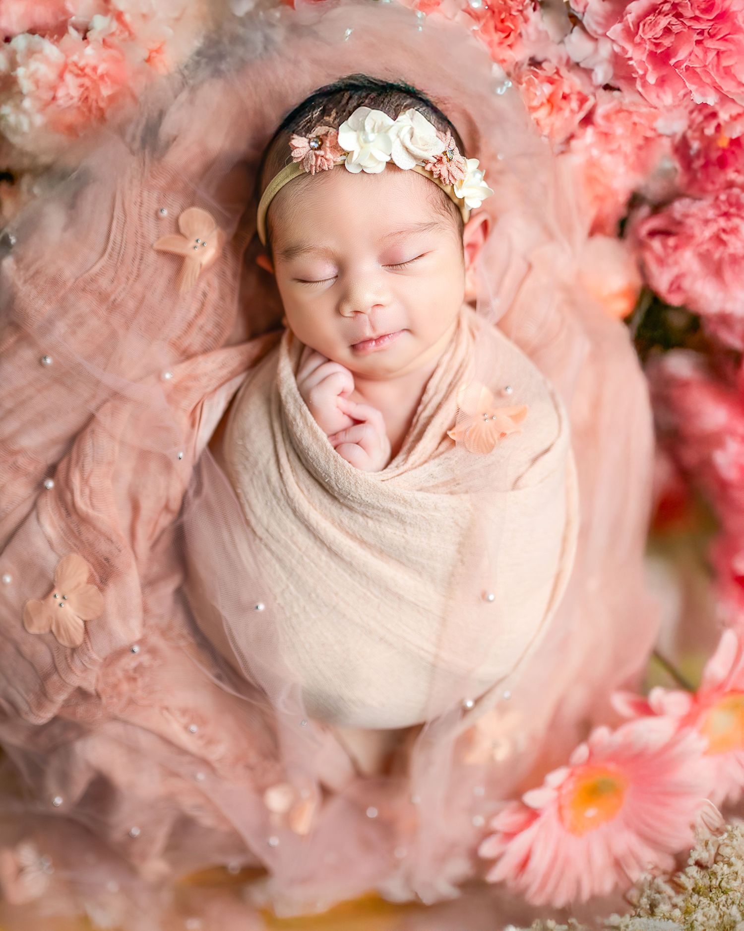 Newborn baby wrapped in cream fabric surrounded by pink flowers and soft lighting in artistic collage.