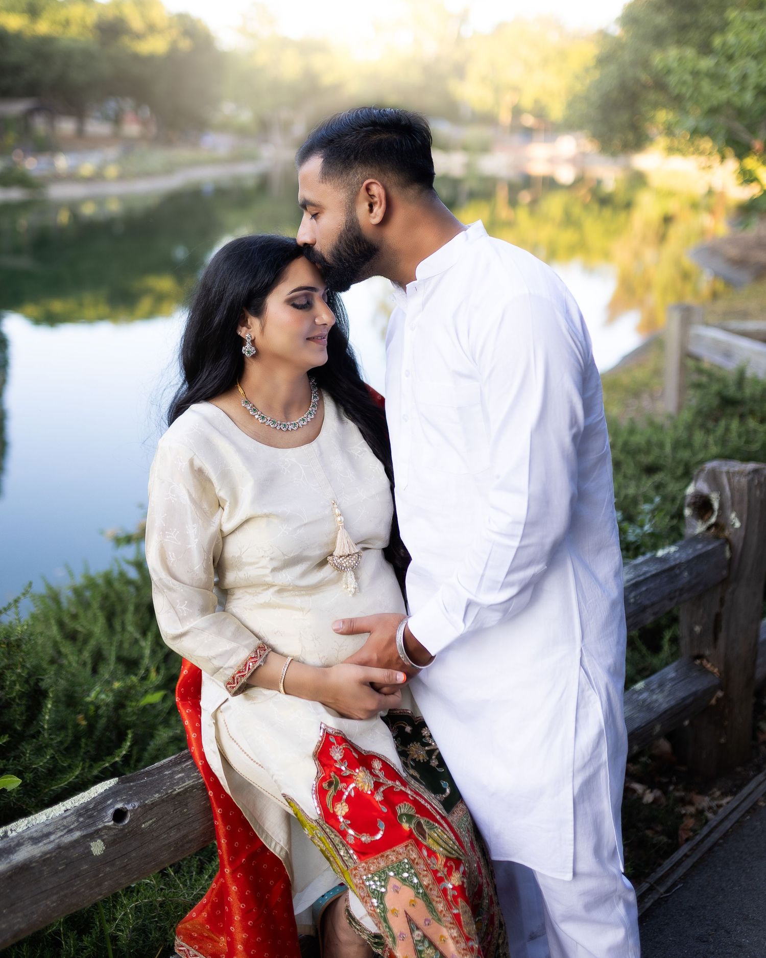 A couple in matching white and red outfits share an intimate moment by a lake during golden hour.