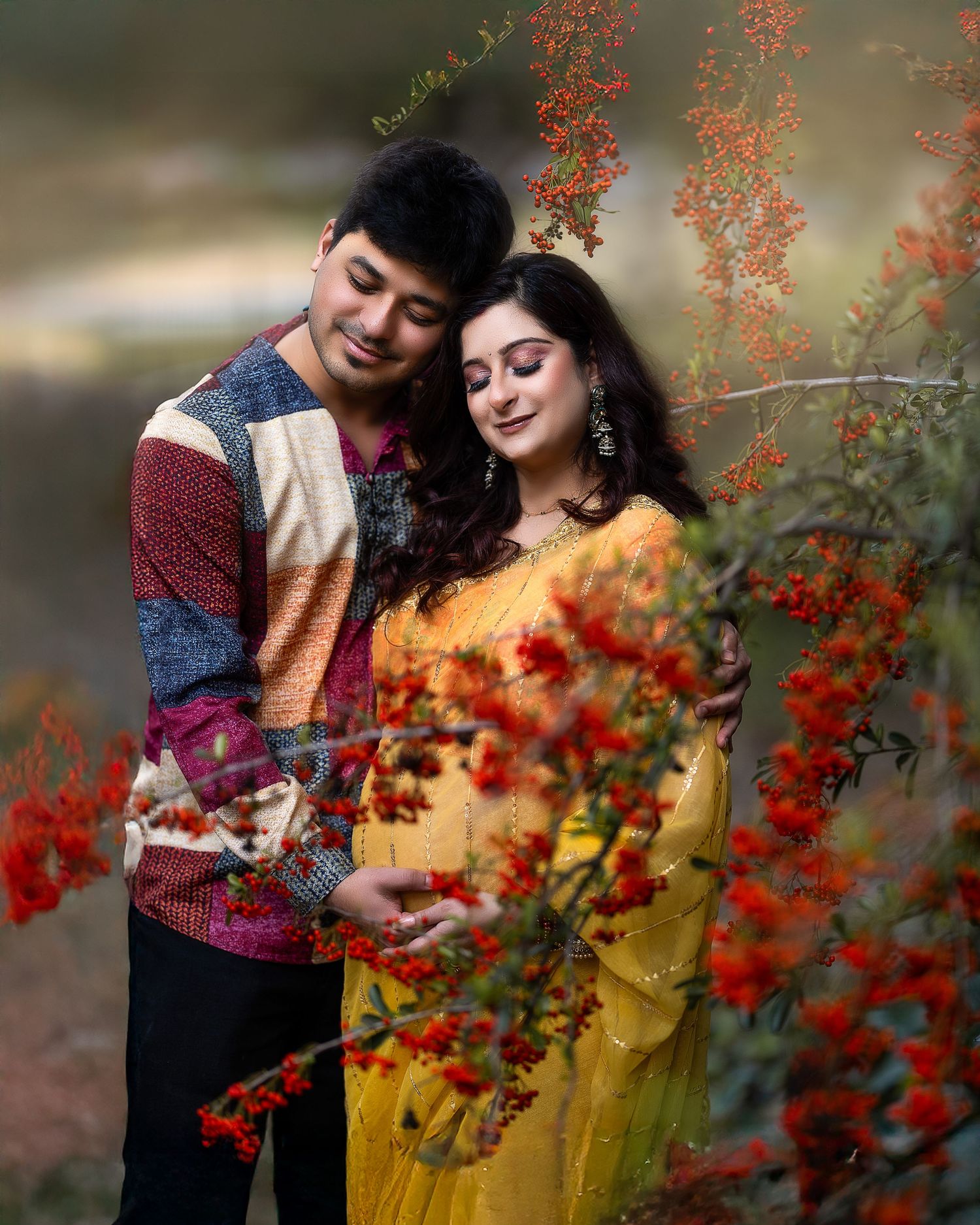 A couple poses romantically among vibrant red berries and autumn foliage during an outdoor photo session.