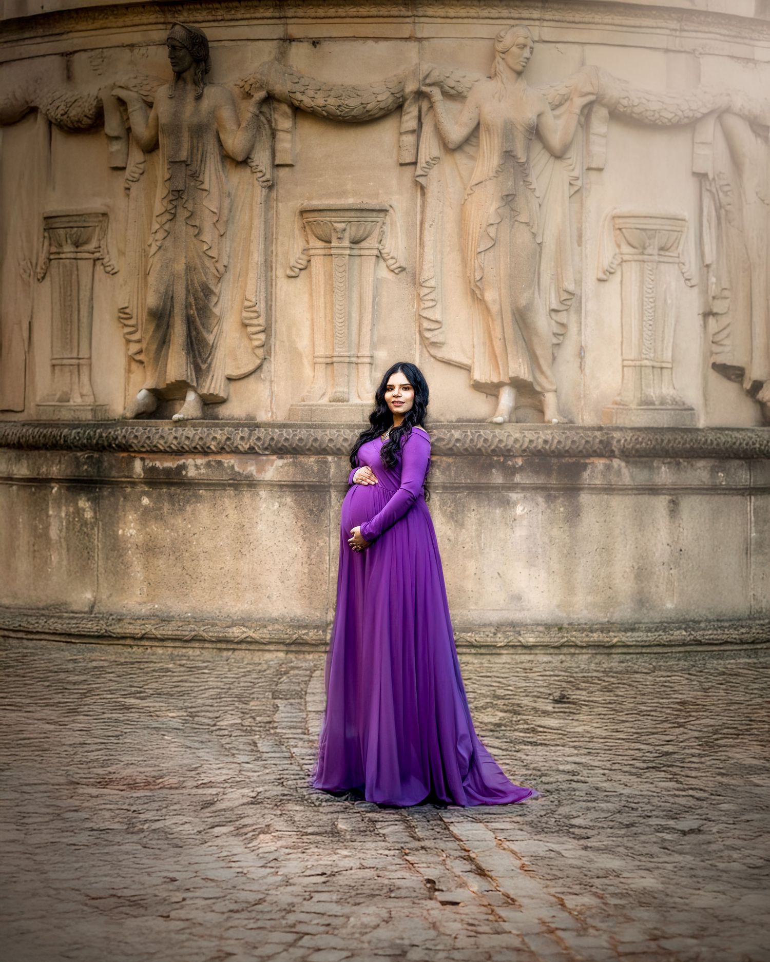 A person in a flowing purple gown poses dramatically against ancient stone walls and cobblestone ground.