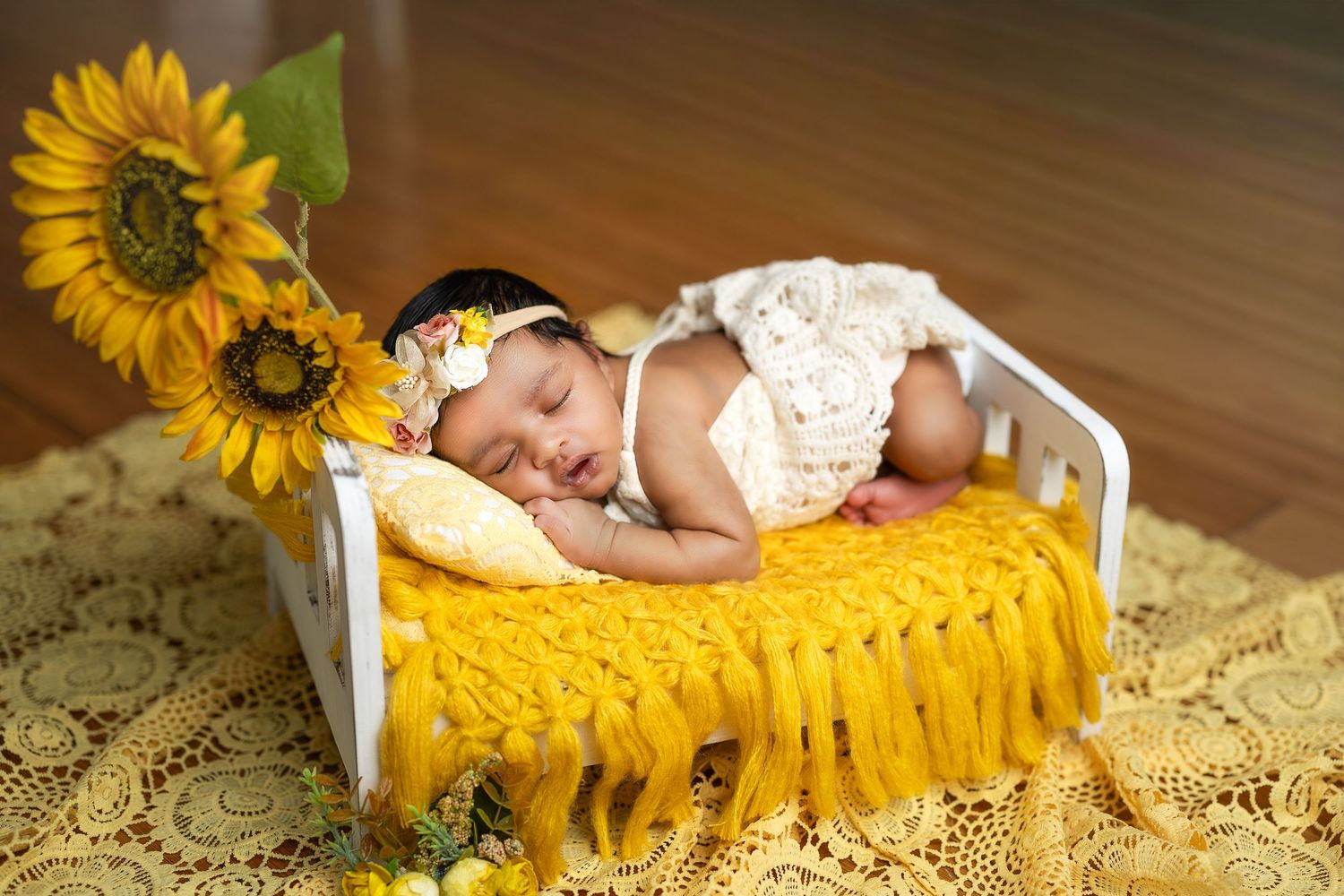 Newborn photography session with sunflowers and yellow blanket on hardwood floor.