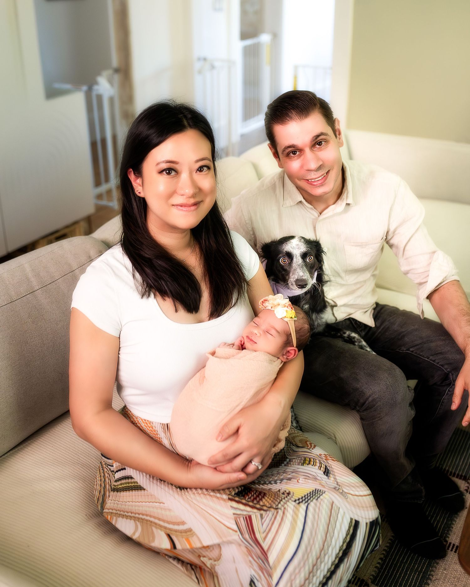 A couple sits on a beige couch with their black and white dog while relaxing at home.