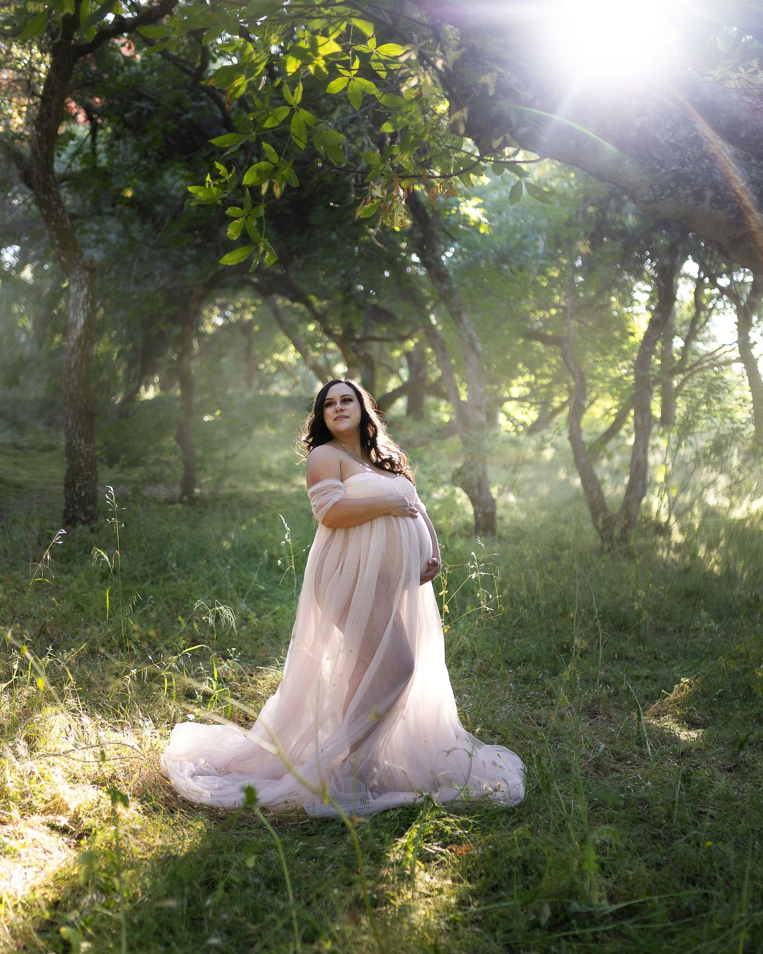 A person in a flowing white dress sits gracefully in a sunlit forest clearing surrounded by lush greenery and dappled light.
