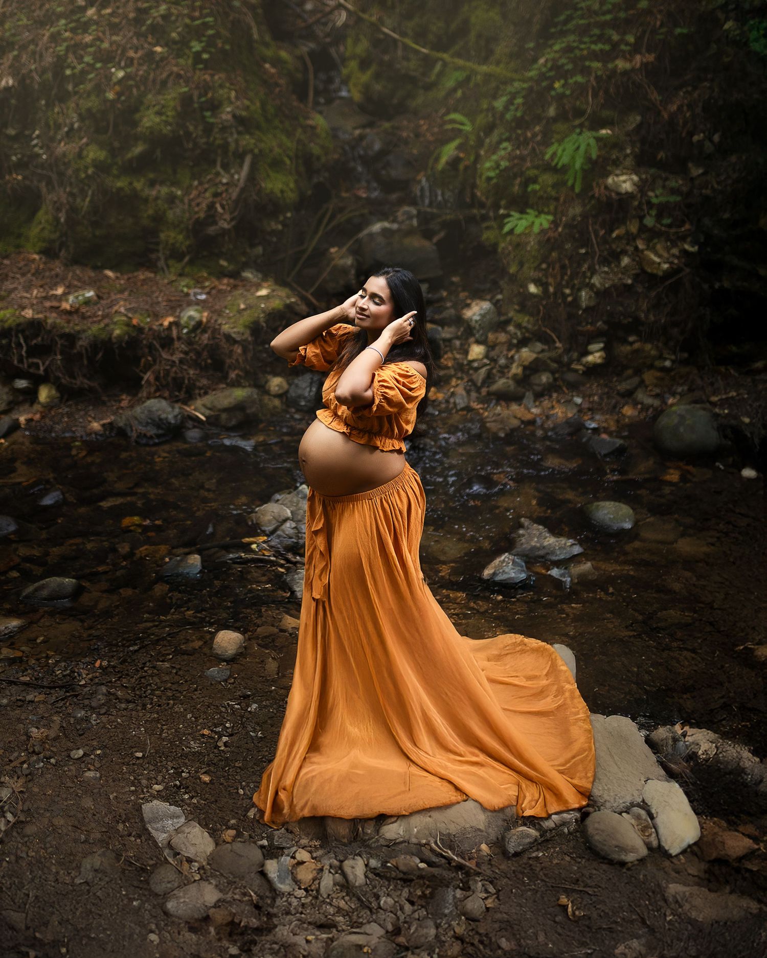 A flowing orange dress creates an artistic movement sequence against a dark rocky creek background.