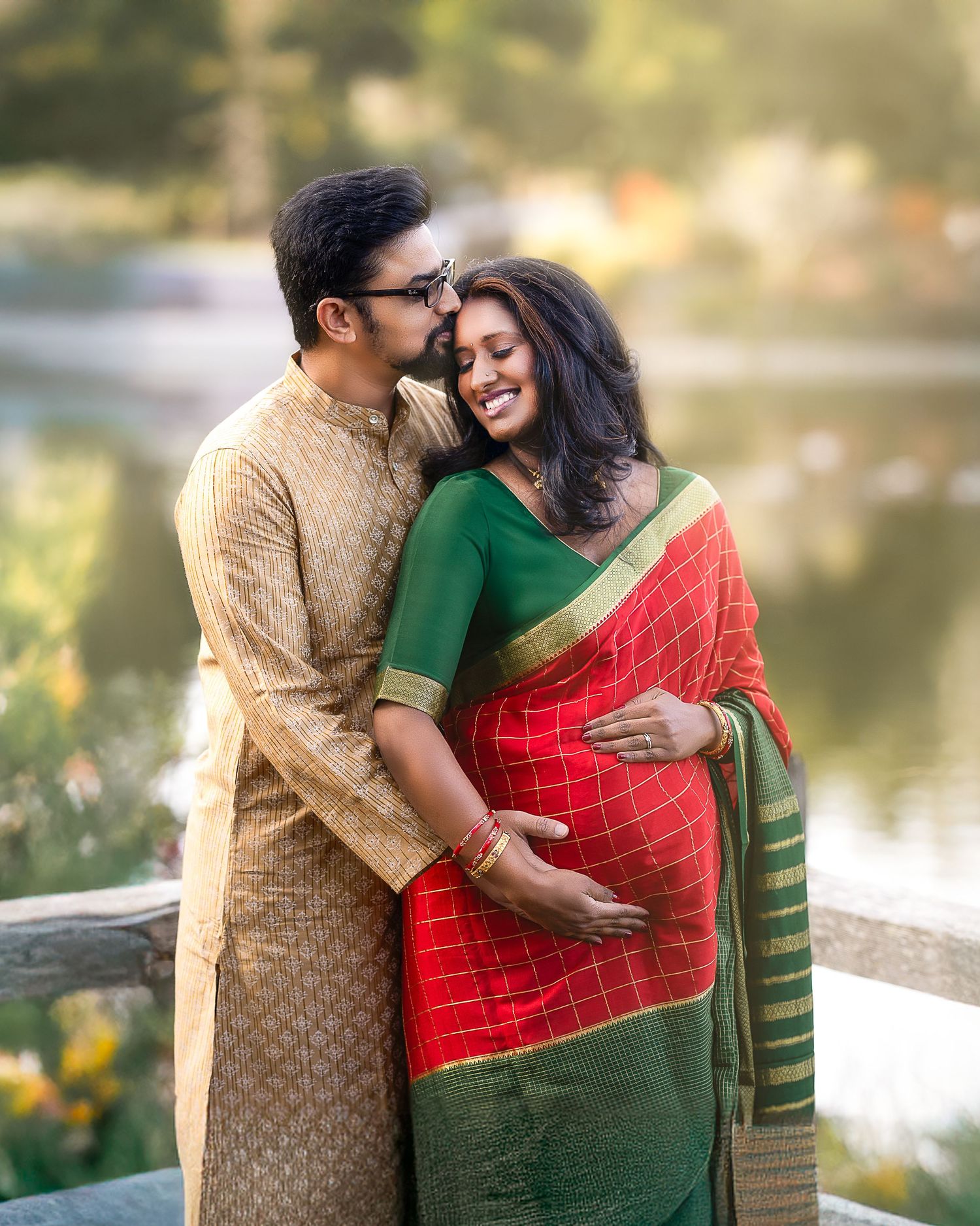 Couple in traditional Indian attire sharing tender moments by a lakeside in warm evening light.