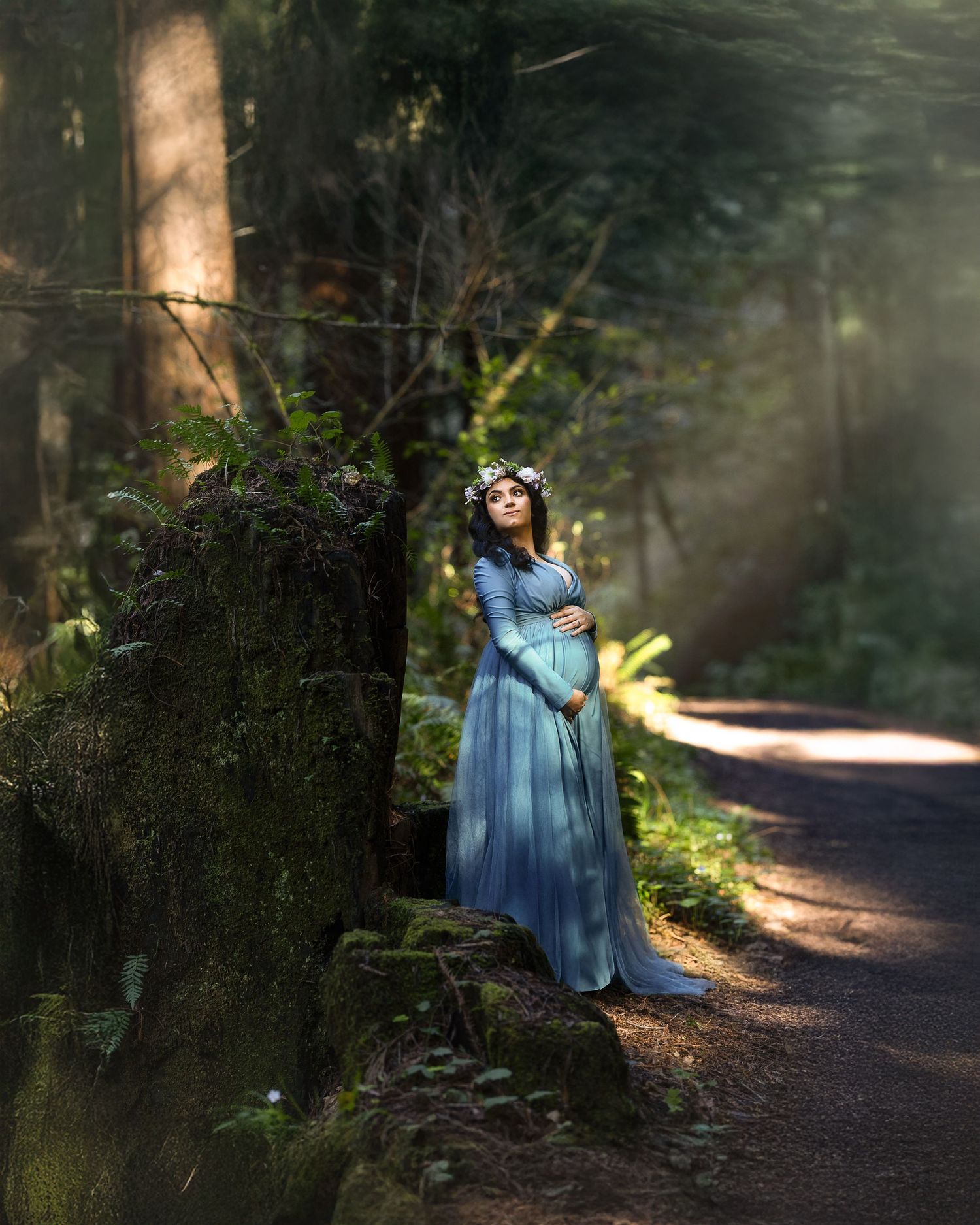 A dreamy forest path with sunlit trees and a figure in a flowing blue dress standing in dappled light.