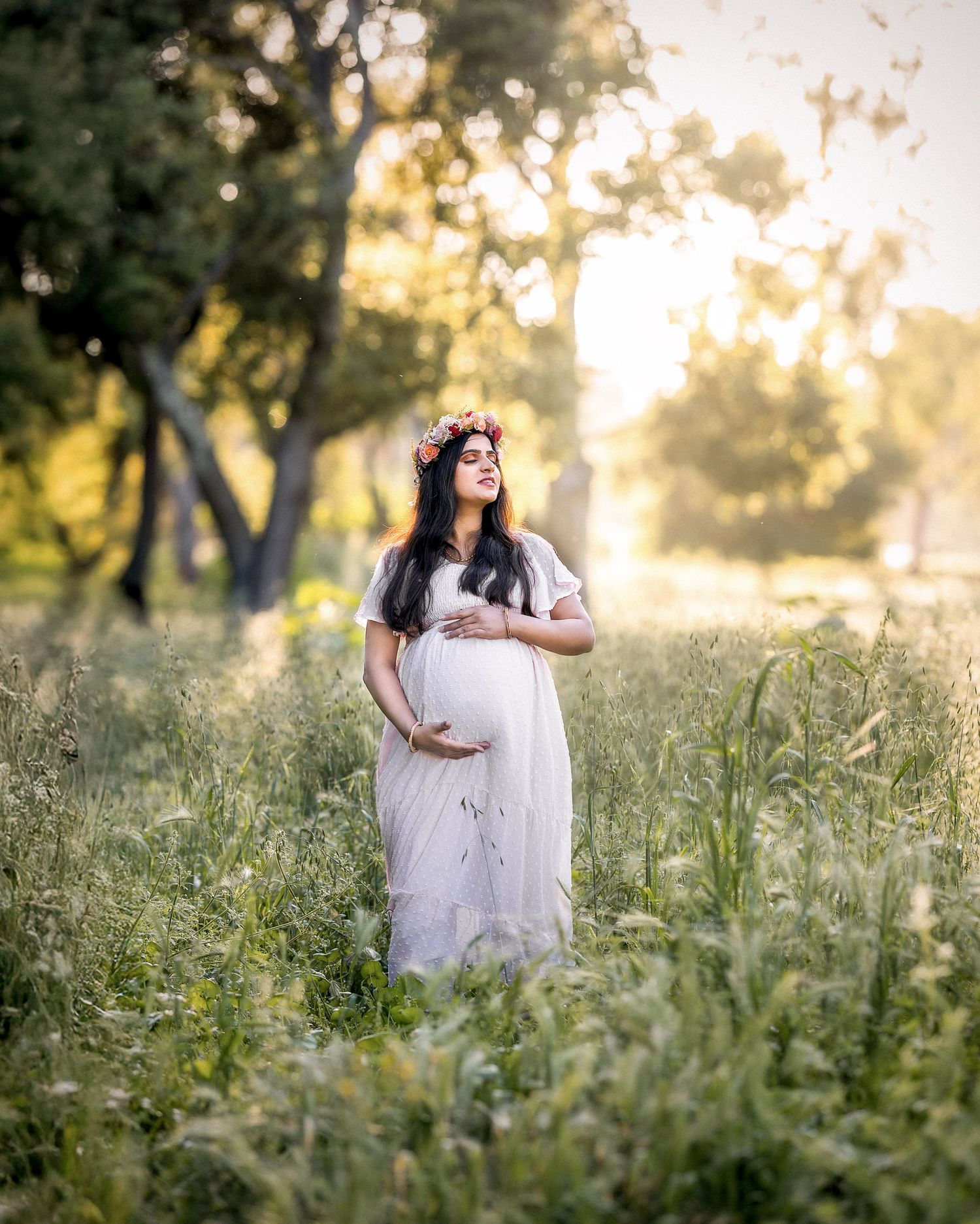 A person in a white dress stands in a sunlit meadow at golden hour with wildflowers and tall grass surrounding them.
