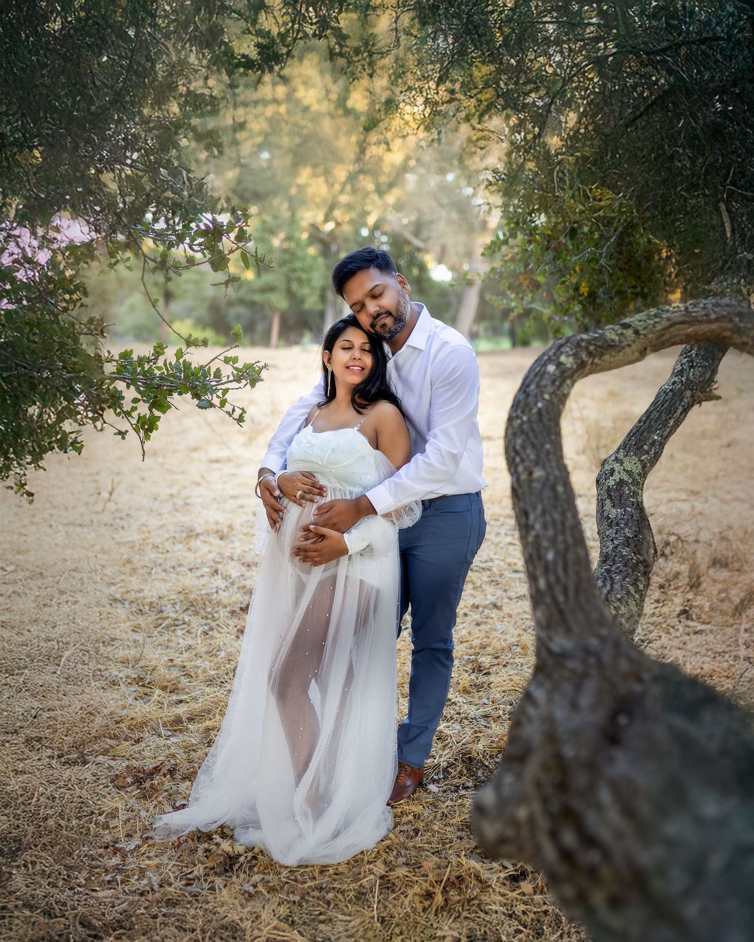A romantic wedding couple shares intimate moments among rustic trees in a dreamy outdoor setting at sunset.