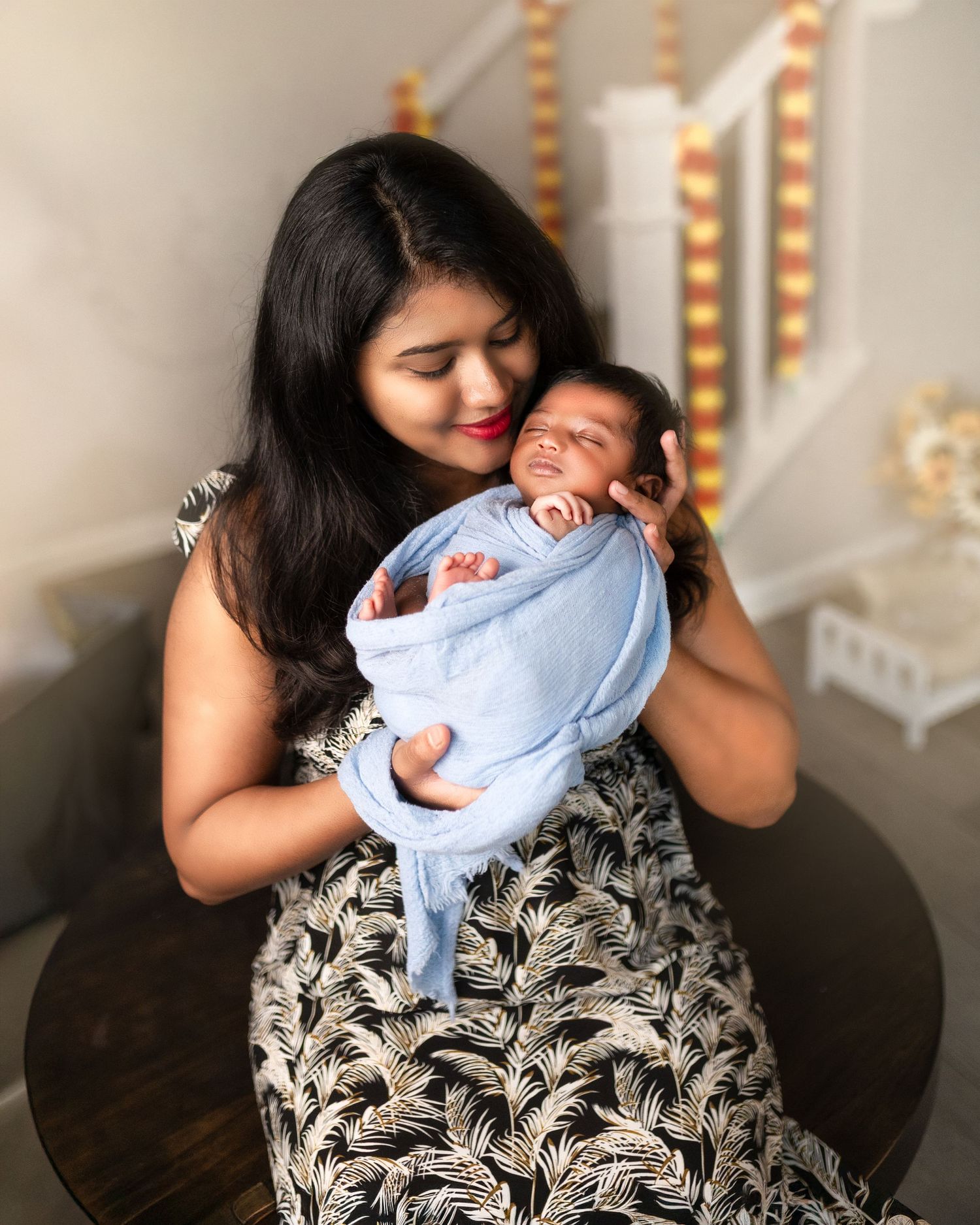 A parent holds and comforts a sleeping baby wrapped in a light blue blanket against a decorative background.