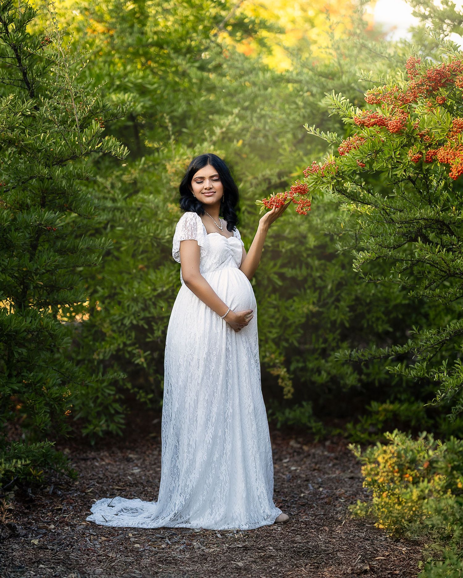 A person in a flowing white dress poses gracefully in a garden setting with vibrant red and yellow flowers.