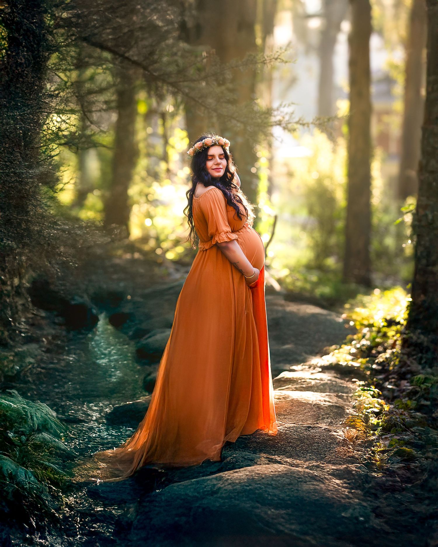 A person wearing a flowing orange dress stands in a sunlit forest setting during a magical photoshoot.