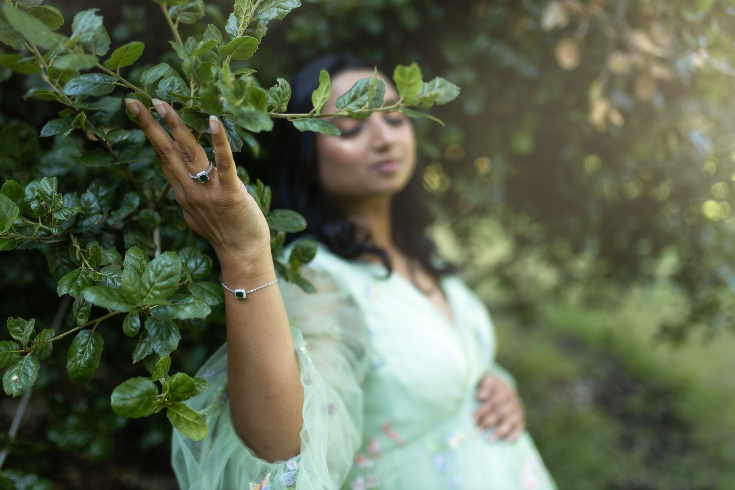 Person in a mint green dress picks fresh fruit from a tree in a lush garden setting.