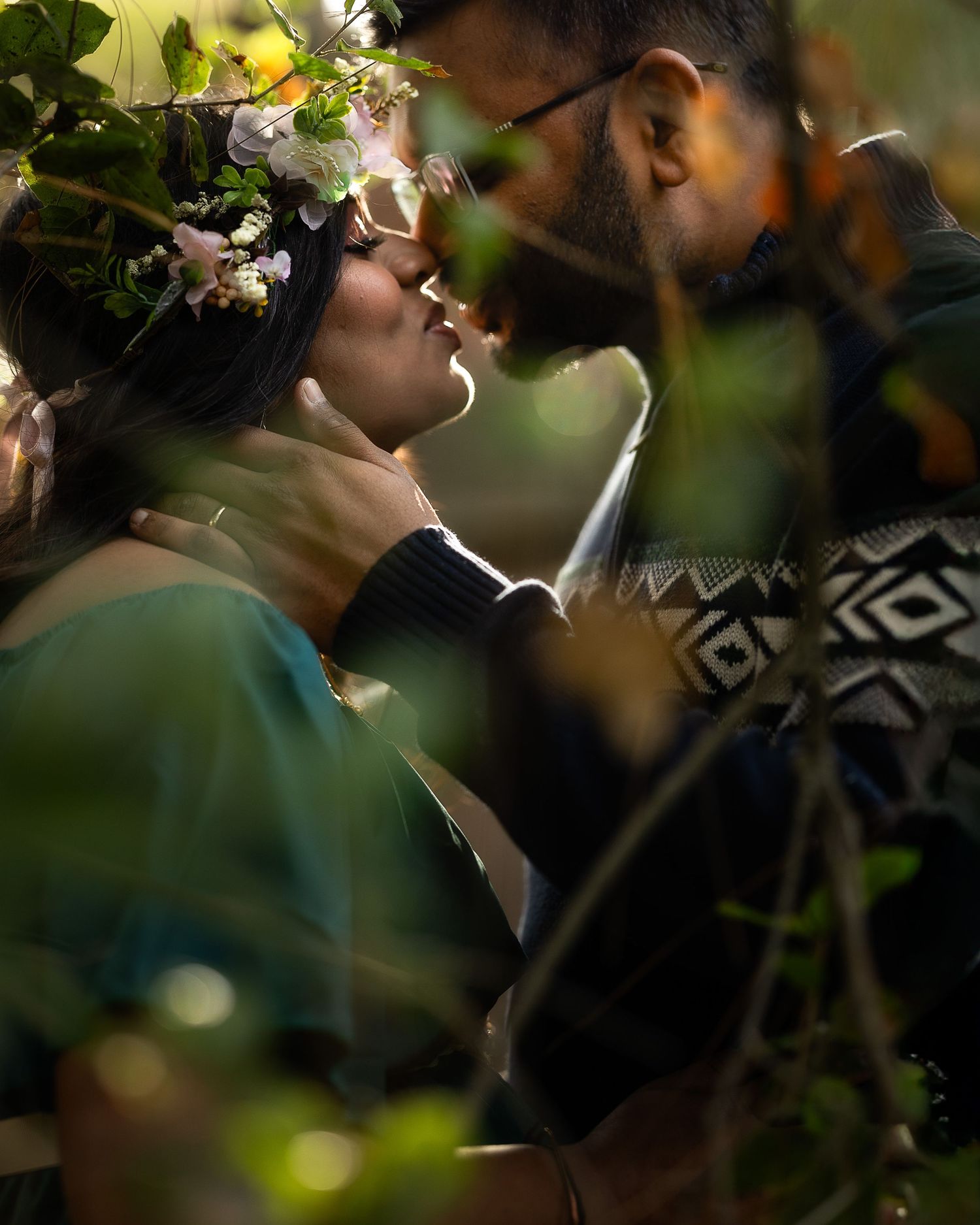 A romantic outdoor photoshoot captures intimate moments between a couple among natural foliage and soft lighting.